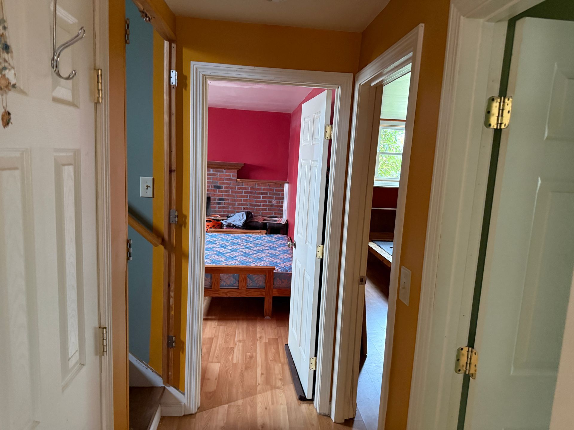 Hallway with open doors leading to a room with bed; walls are various colors: yellow, blue, pink, and white.
