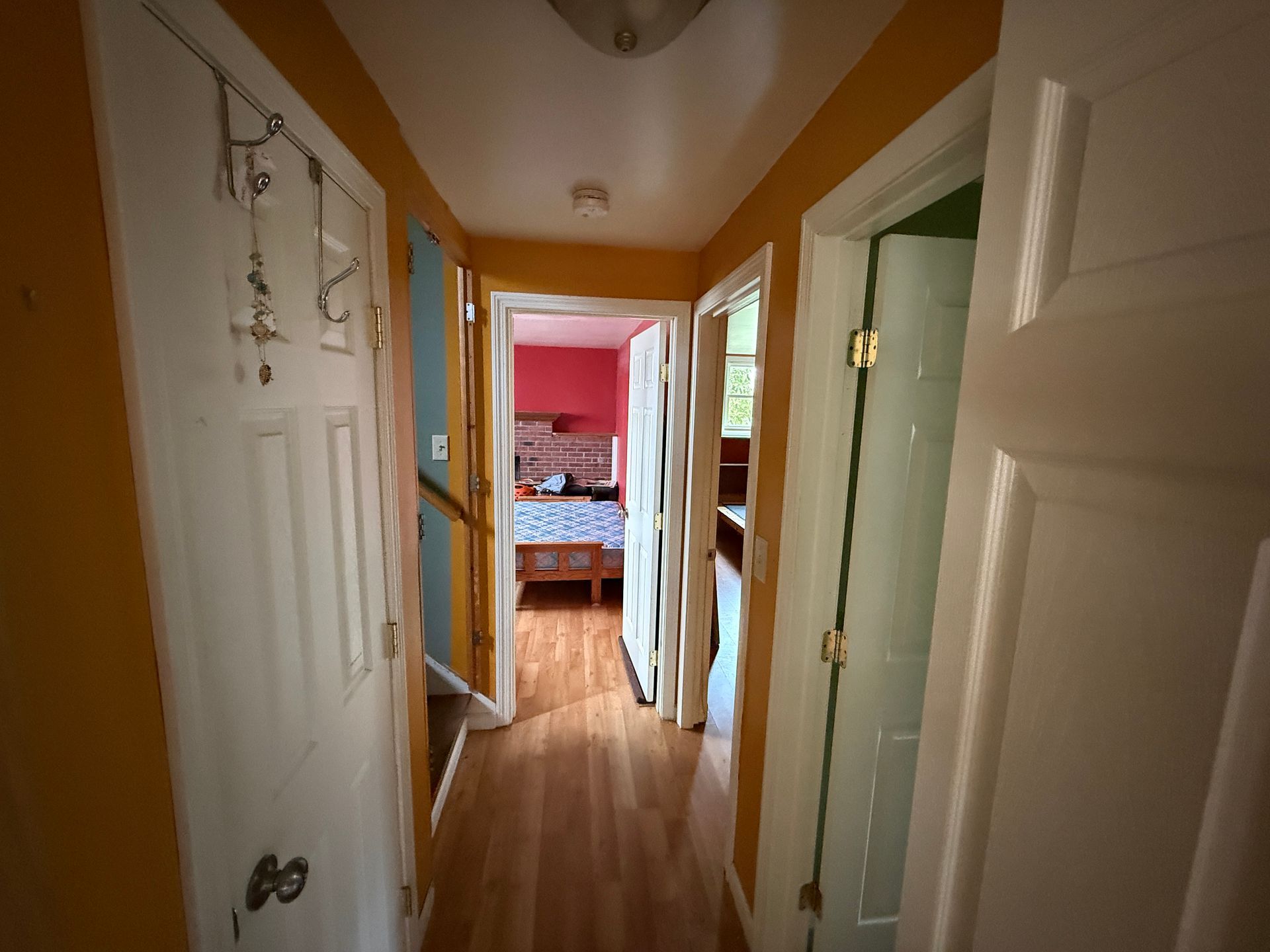 Hallway with white doors, orange walls, and a view into a pink bedroom.