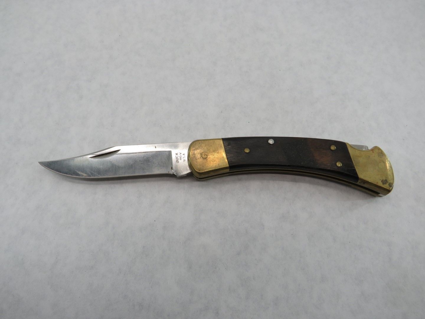 Pocket knife with a stainless steel blade and dark wood handle with brass bolsters.