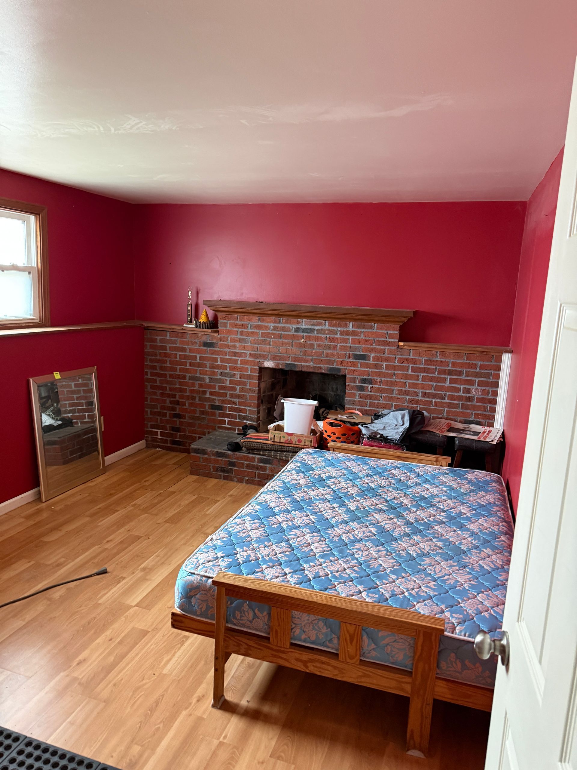 Bedroom with a bed, fireplace, and red walls.  Flooring is wood-look laminate.