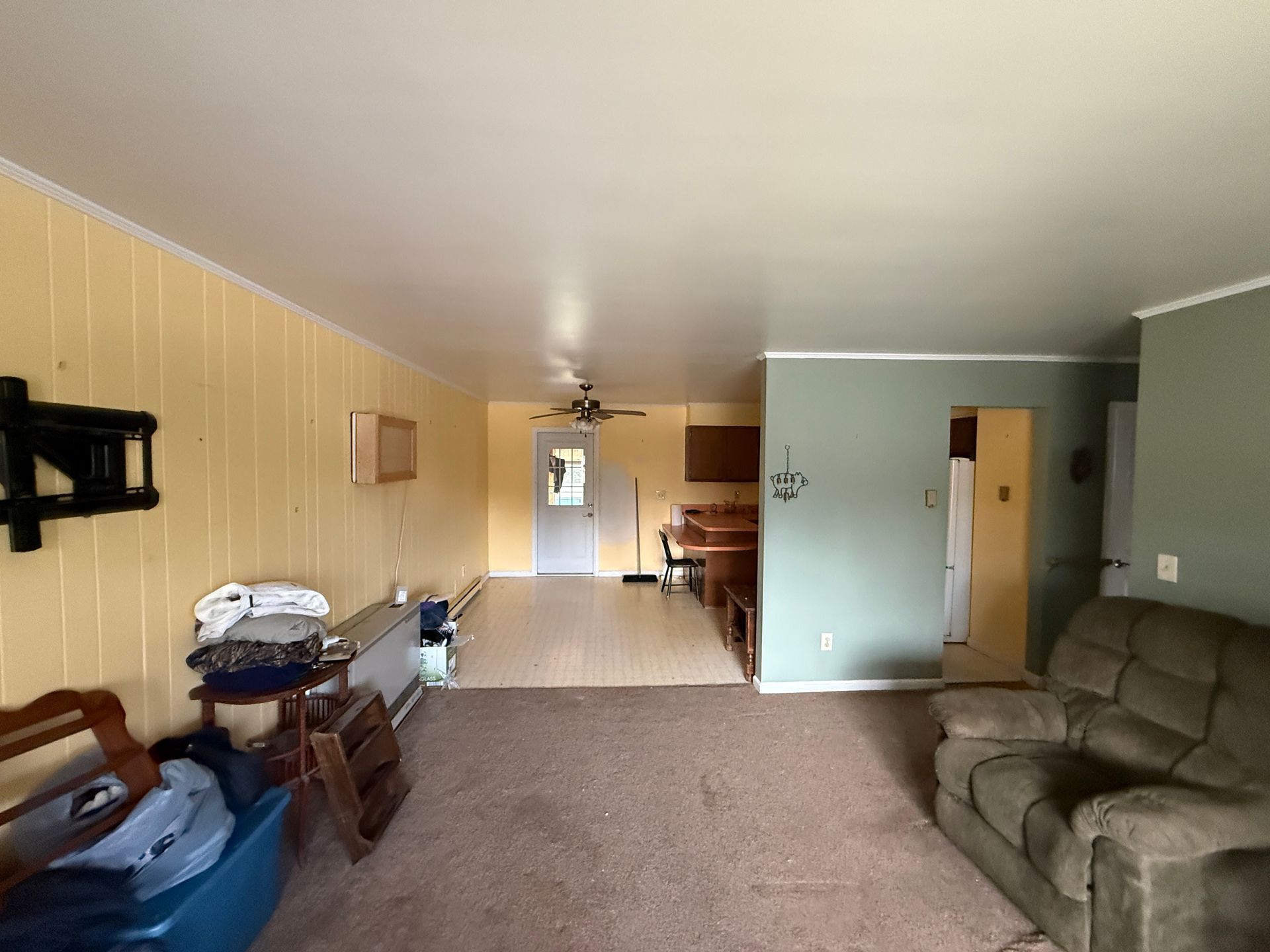 Empty living room with tan carpet, yellow and green walls, and a brown sofa.