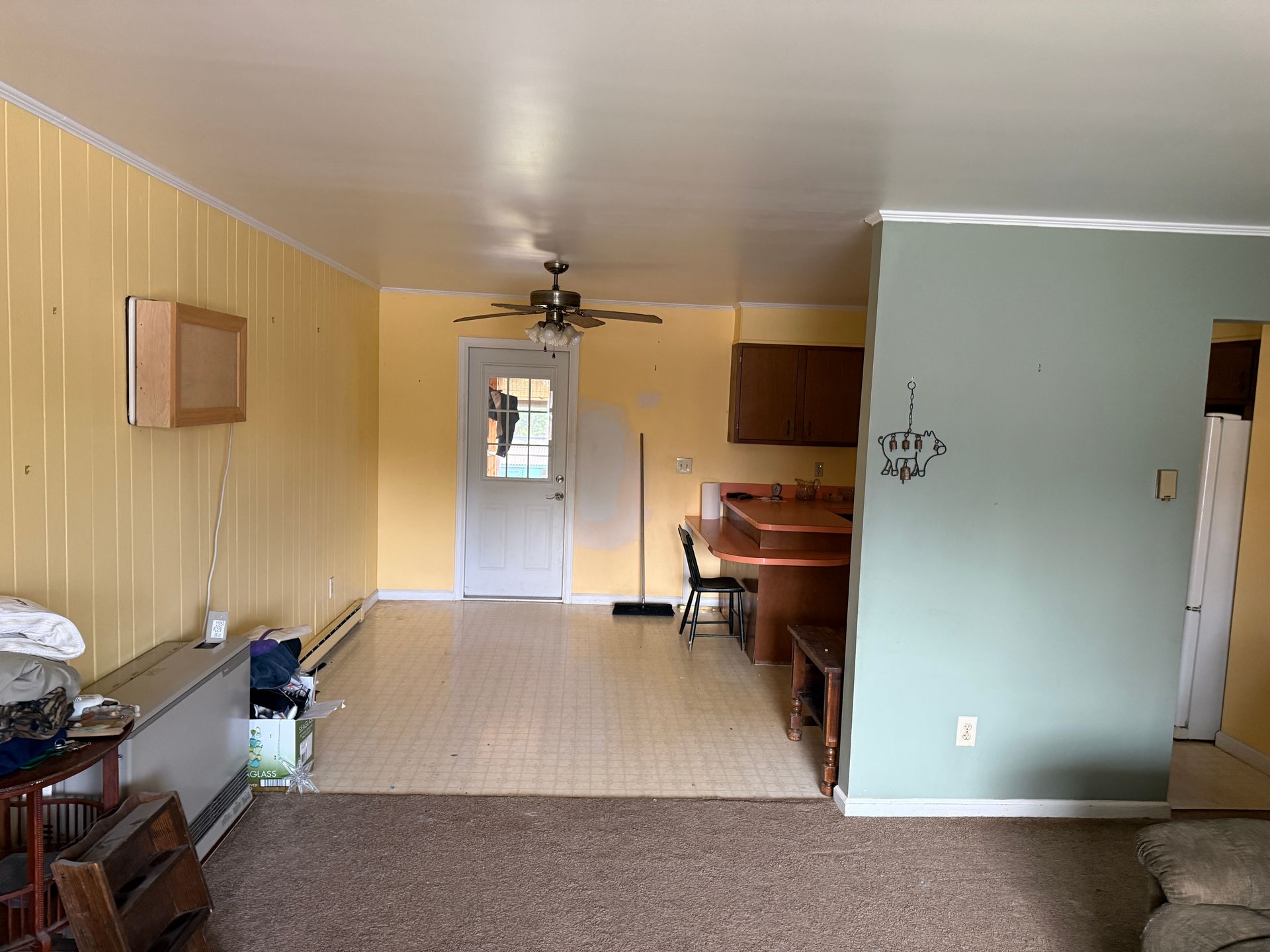 Empty living space with yellow and green walls, tile floor, door to the outside, and a small kitchen.