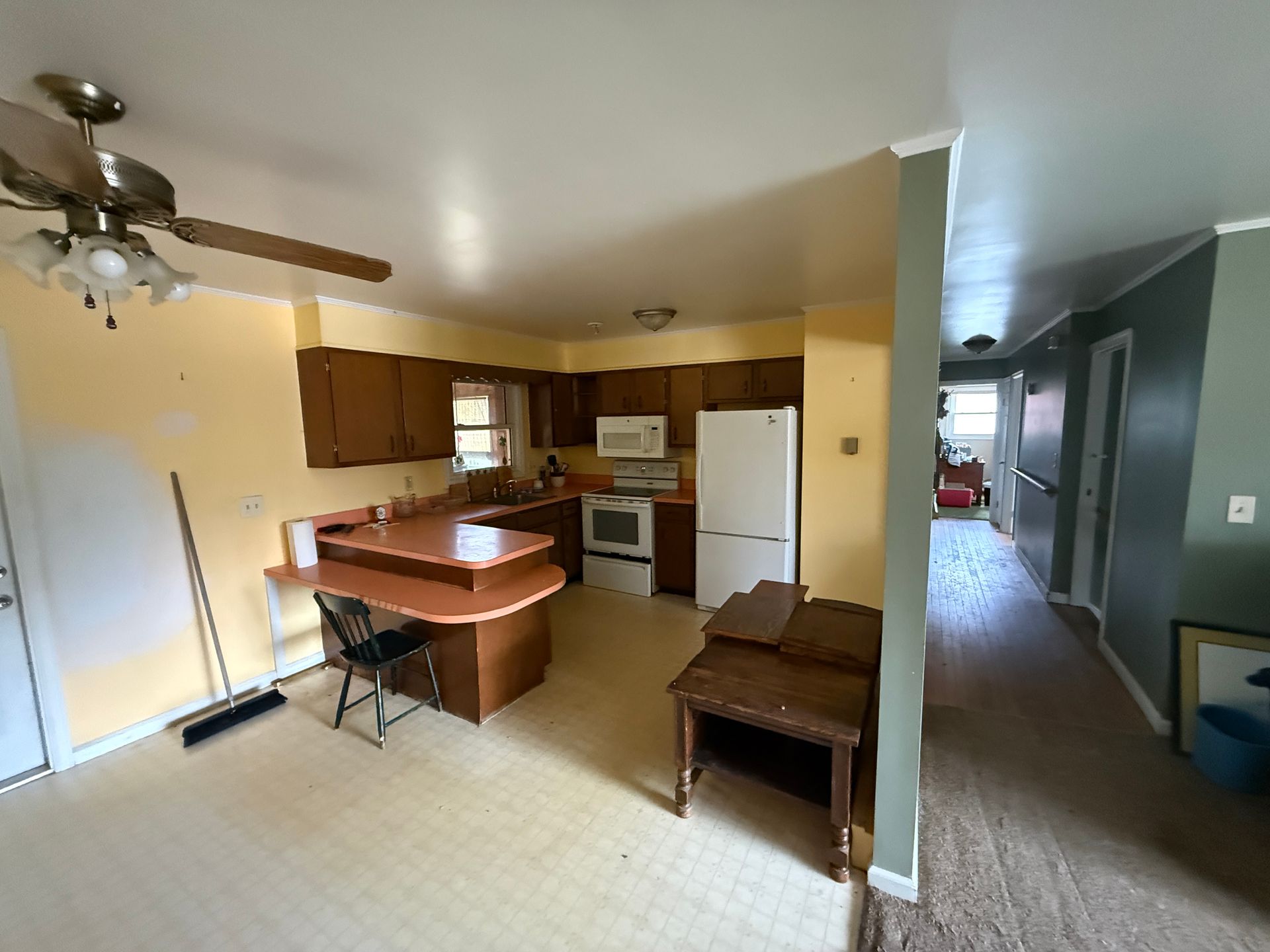 Kitchen with wood cabinets, white appliances, and a small island. Beige and yellow walls, brown flooring.