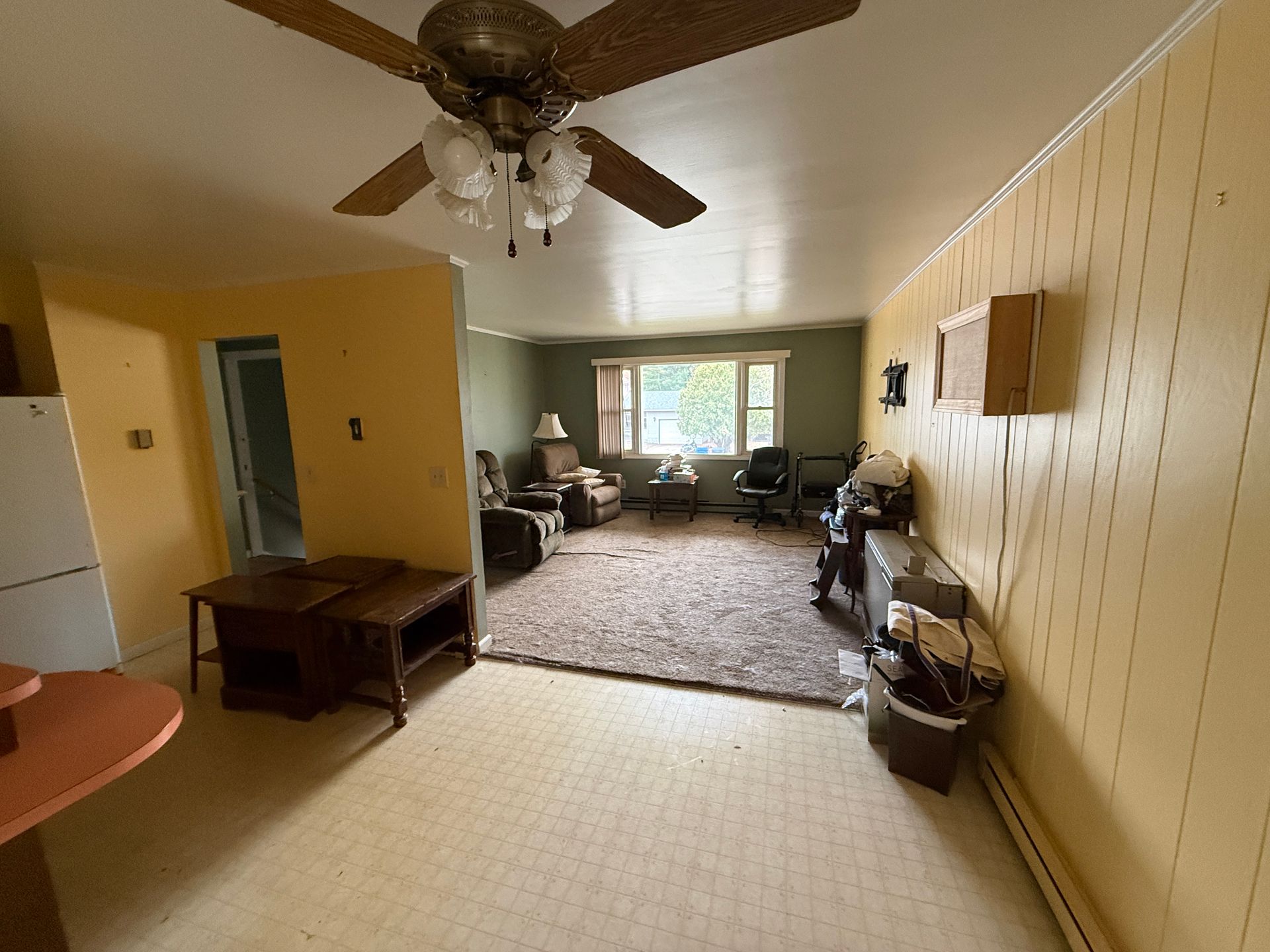 Living room with a ceiling fan, window, and furniture on a patterned rug and floor. Yellow walls.