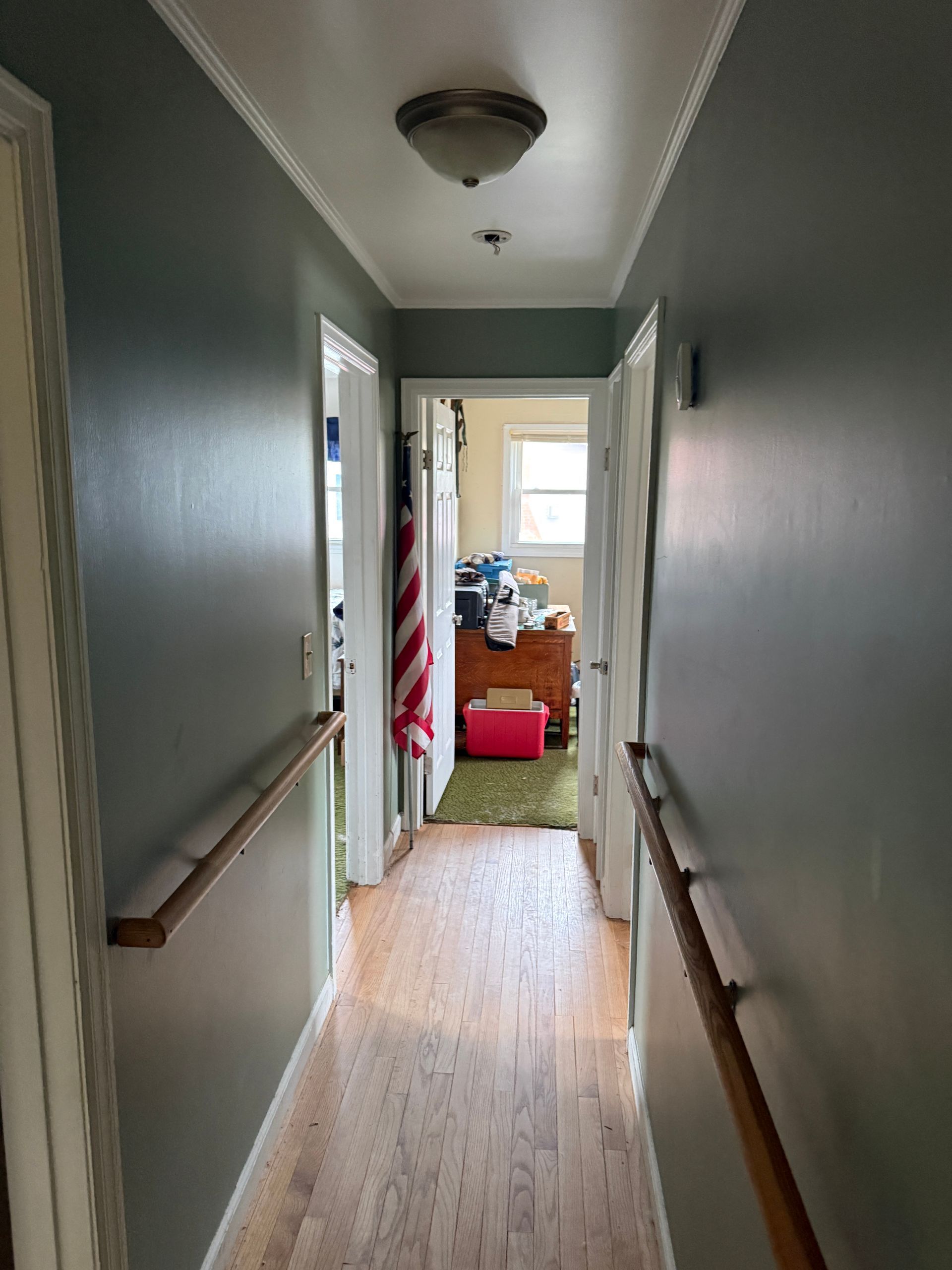 Narrow hallway with light green walls, wood floors, and doors leading to rooms.