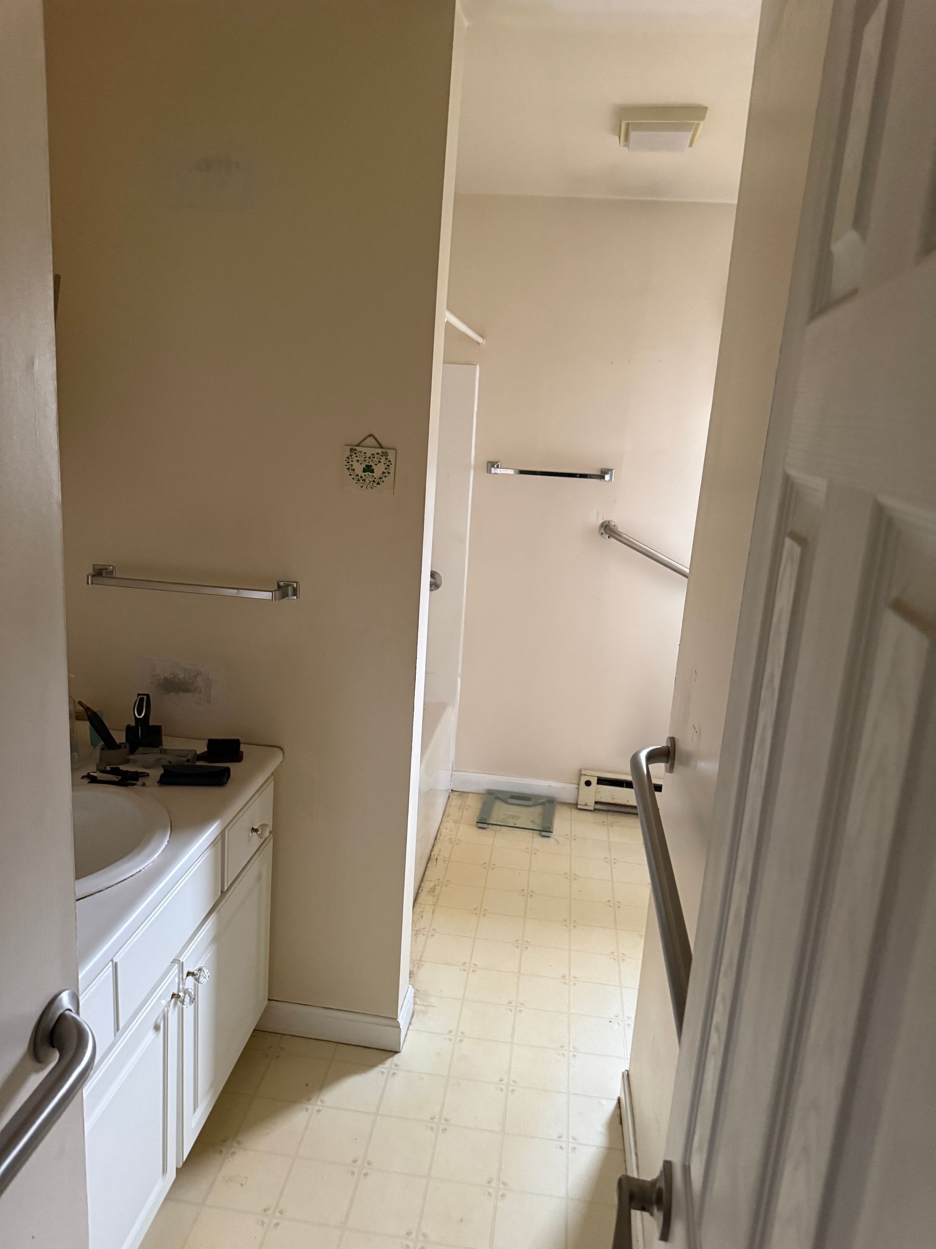 Bathroom with white cabinets, beige walls, and a shower area visible. Door is open.