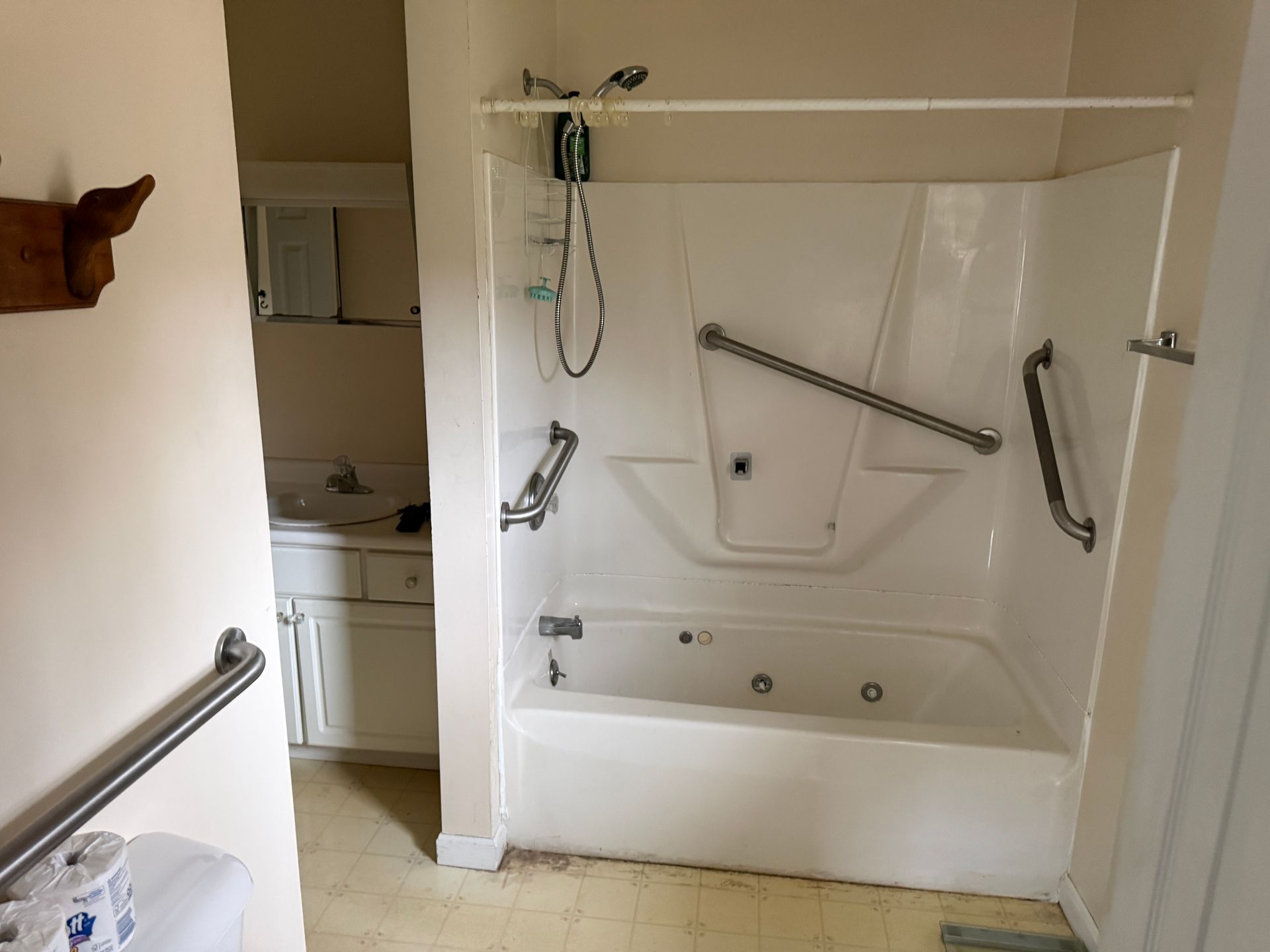Bathroom with white tub and grab bars. Sink and mirror visible in the background.