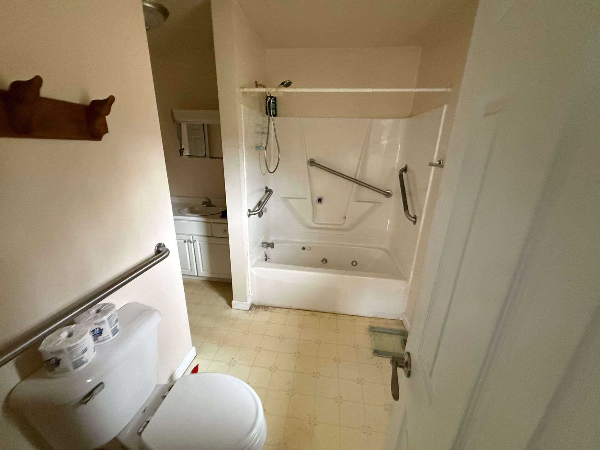 Bathroom with a toilet, tub/shower, and sink, including grab bars for accessibility.