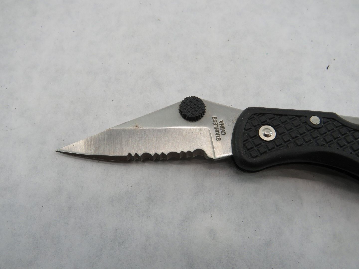 Close-up of a serrated folding knife with a black handle.