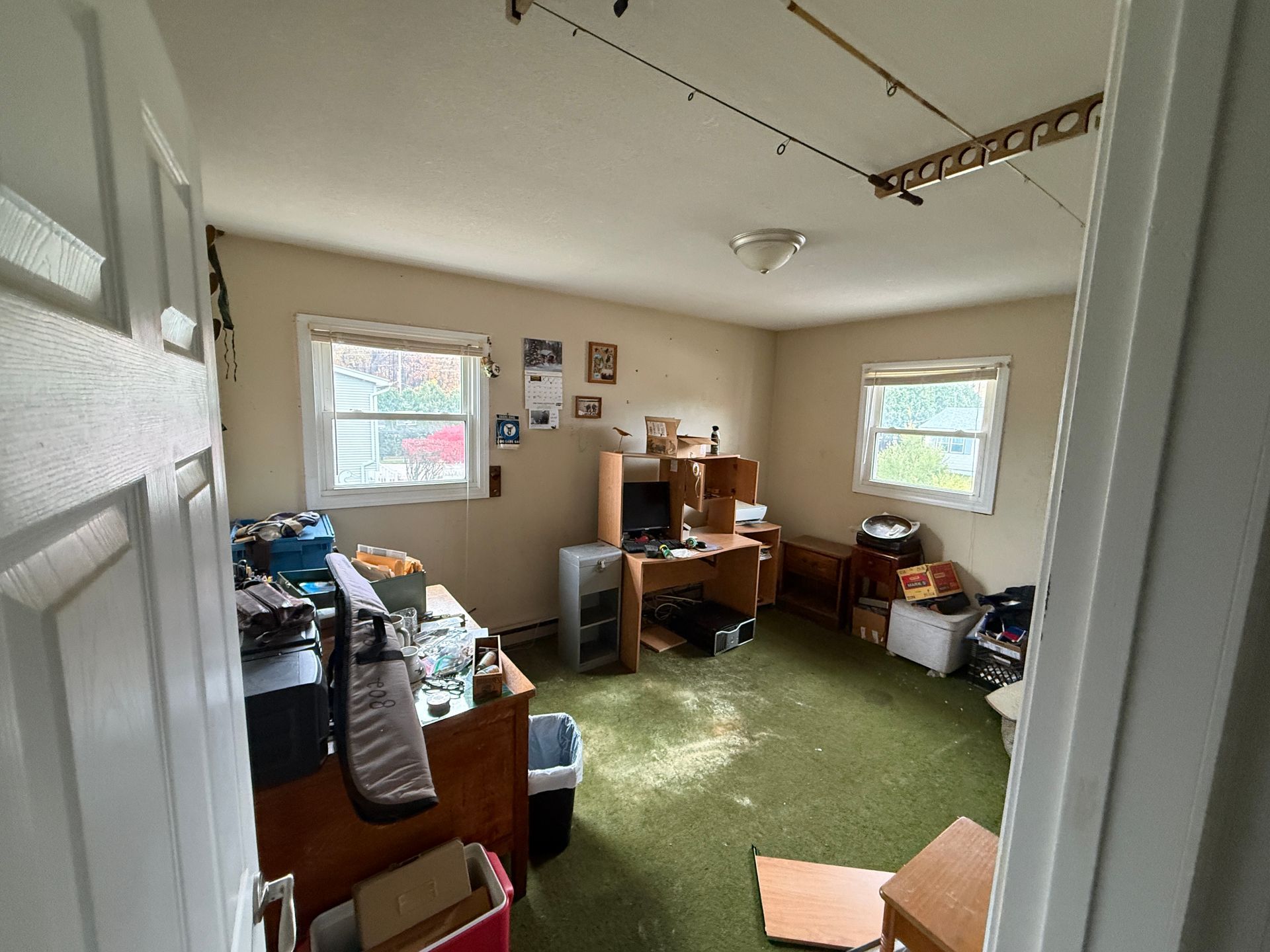 An office room with a desk, windows, and green carpet. A door is partially open.