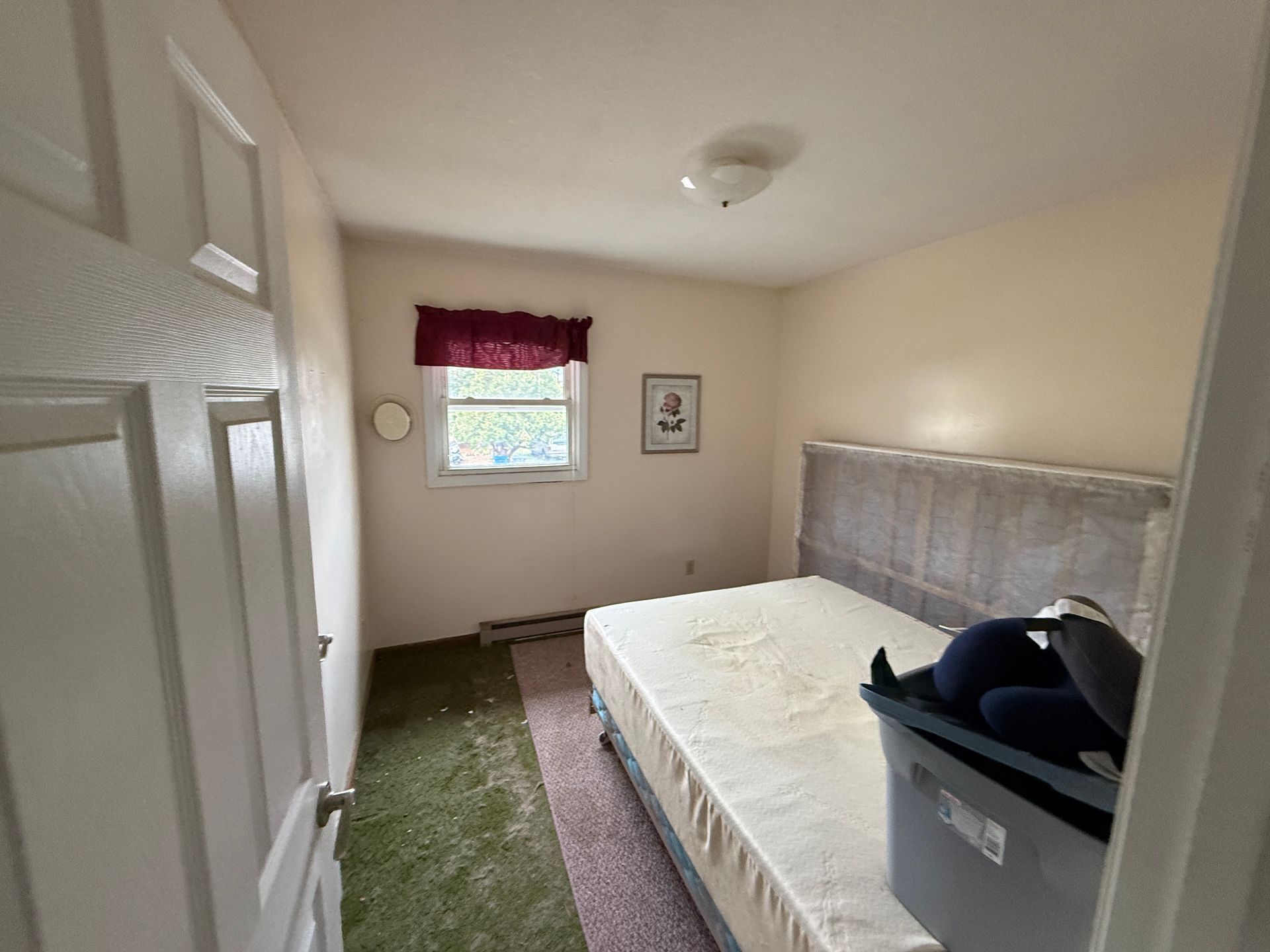 Bedroom with bed, window, and open door. Walls are beige, carpet is green/brown.
