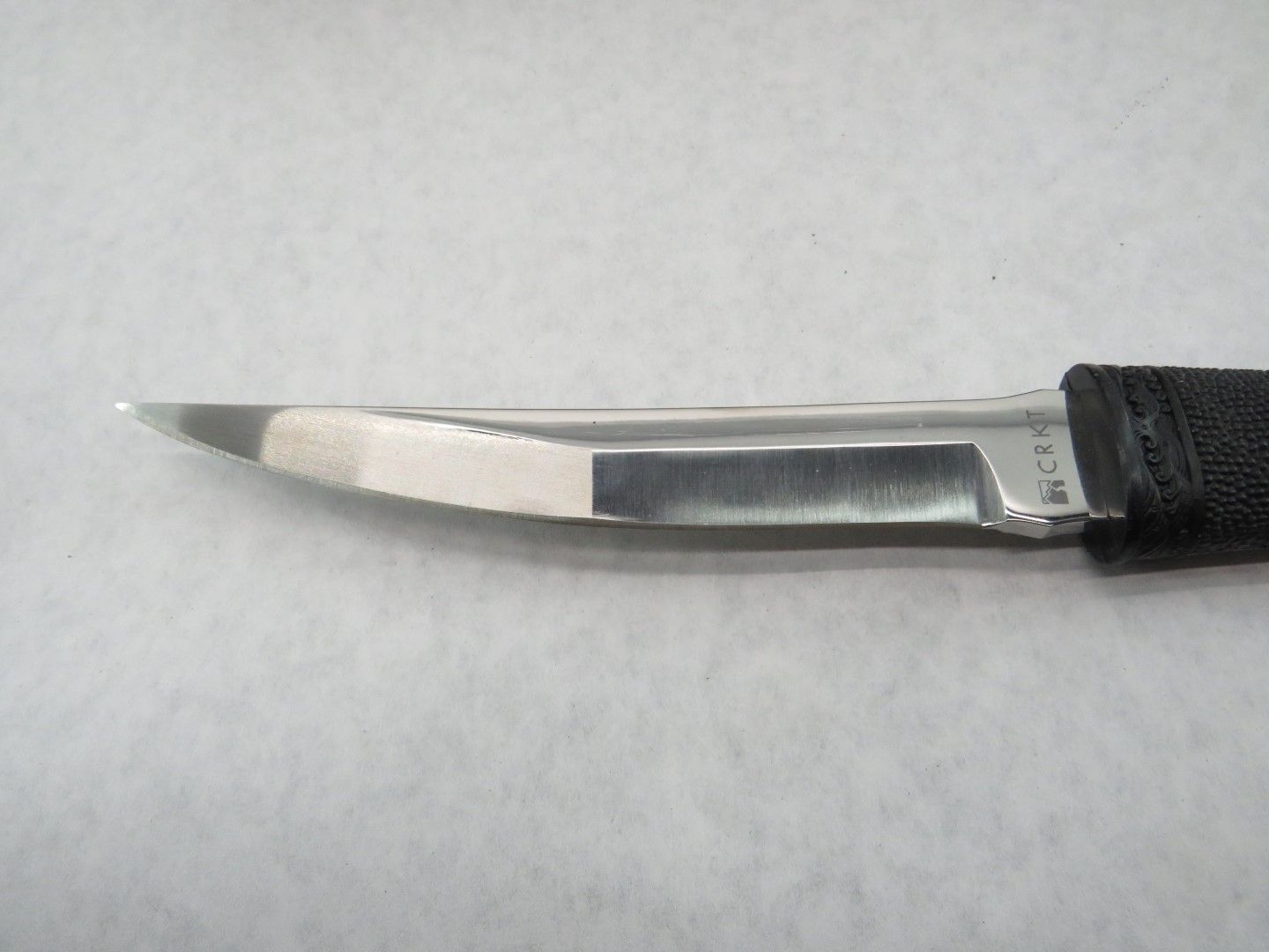 Close-up of a silver knife blade with a black handle, angled against a white background.