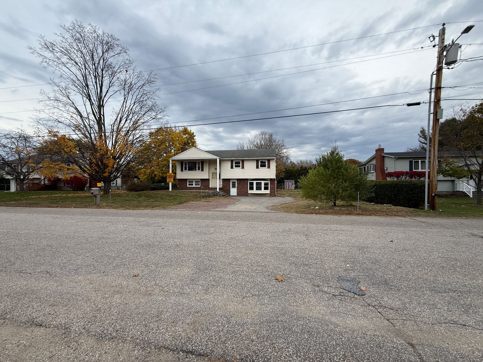 Two-story white house with brown brick, gravel driveway, overcast sky, power pole on right.