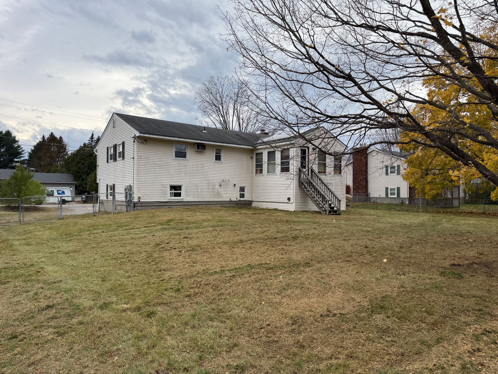 Back of a white house with a grassy lawn on a cloudy day, fall foliage in the trees.