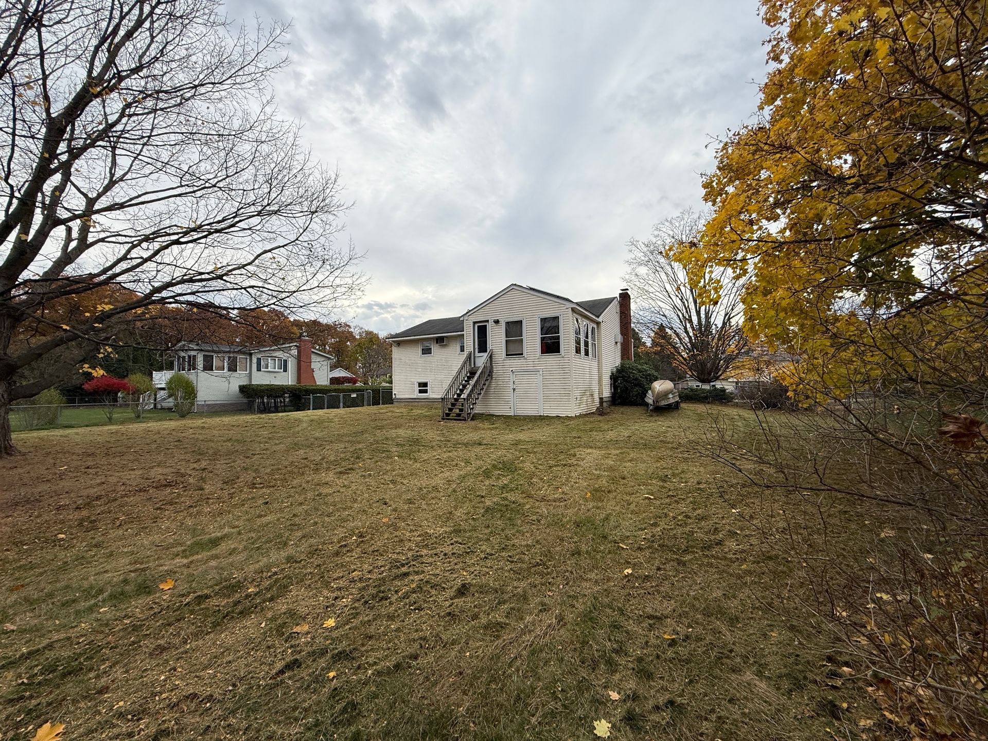 A rundown, white house with a partially collapsed facade, set on a grassy hill with trees in autumn.