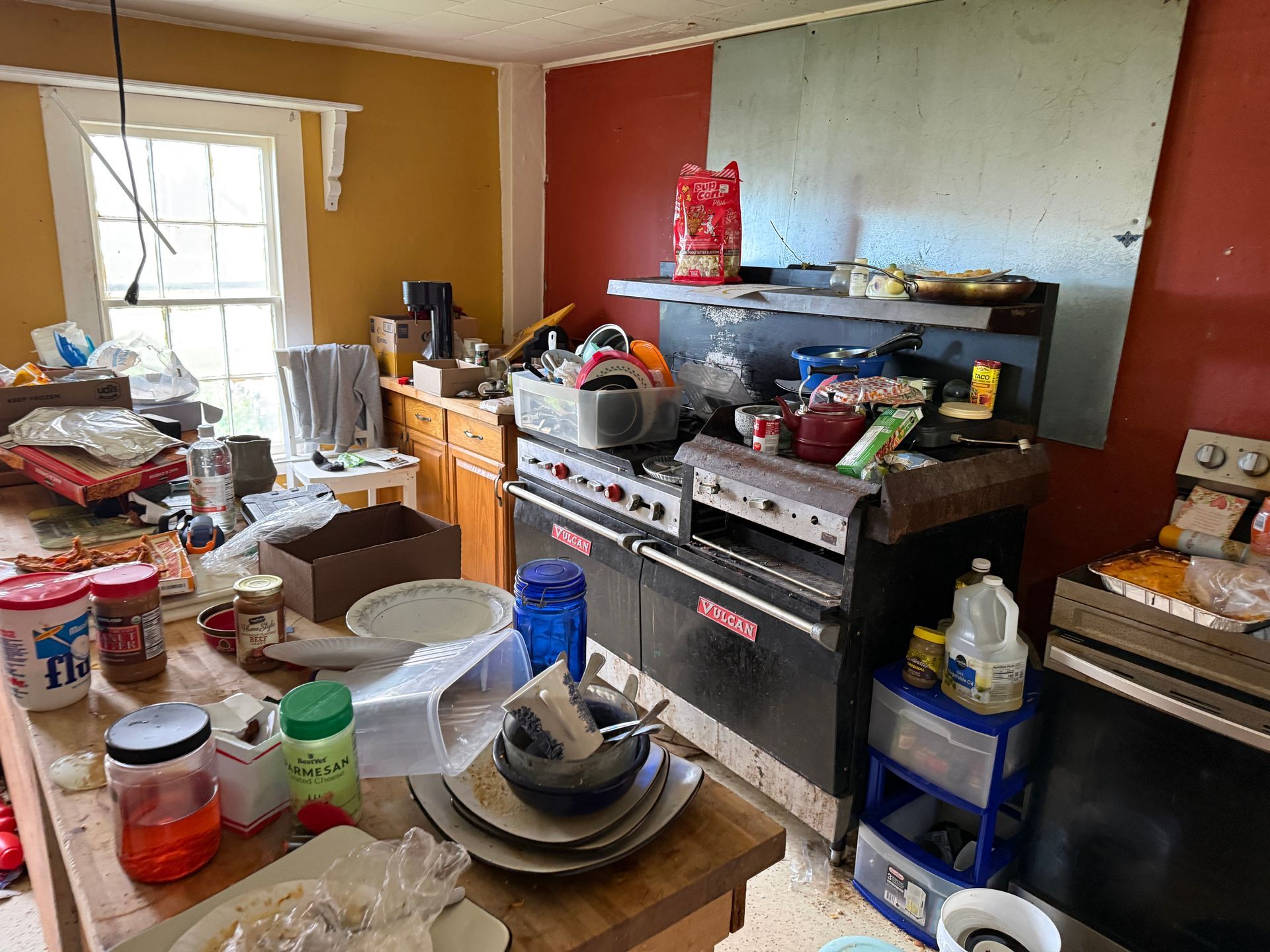Kitchen with appliances and counters, window to the left, red and yellow walls.