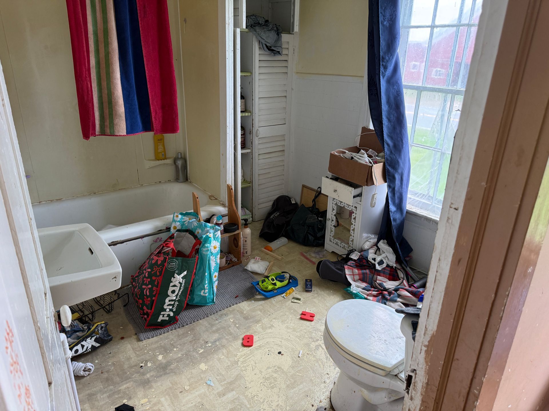 Bathroom with tub, toilet, next to a window with blue curtains.