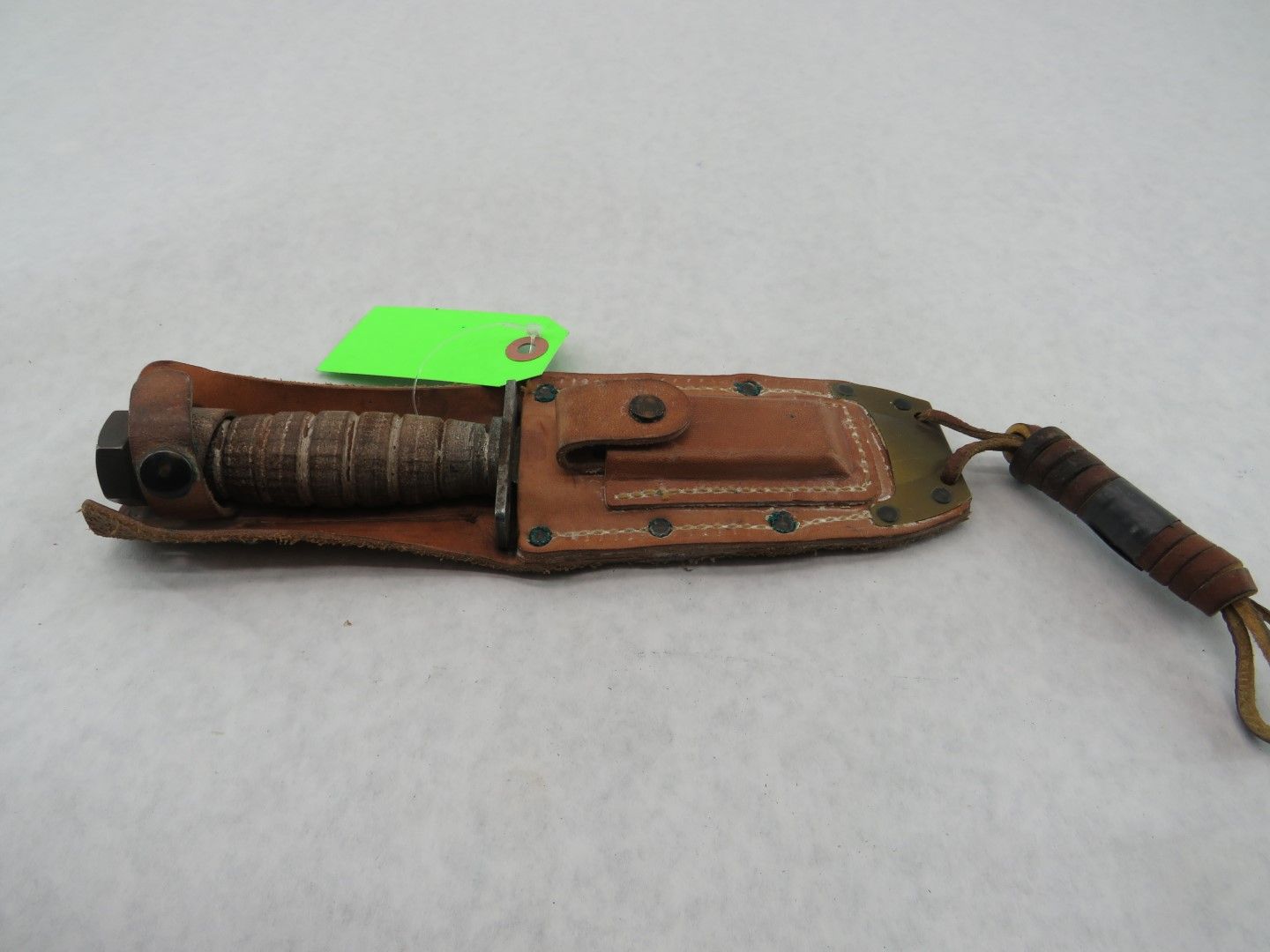 Knife in a leather sheath with a green tag.