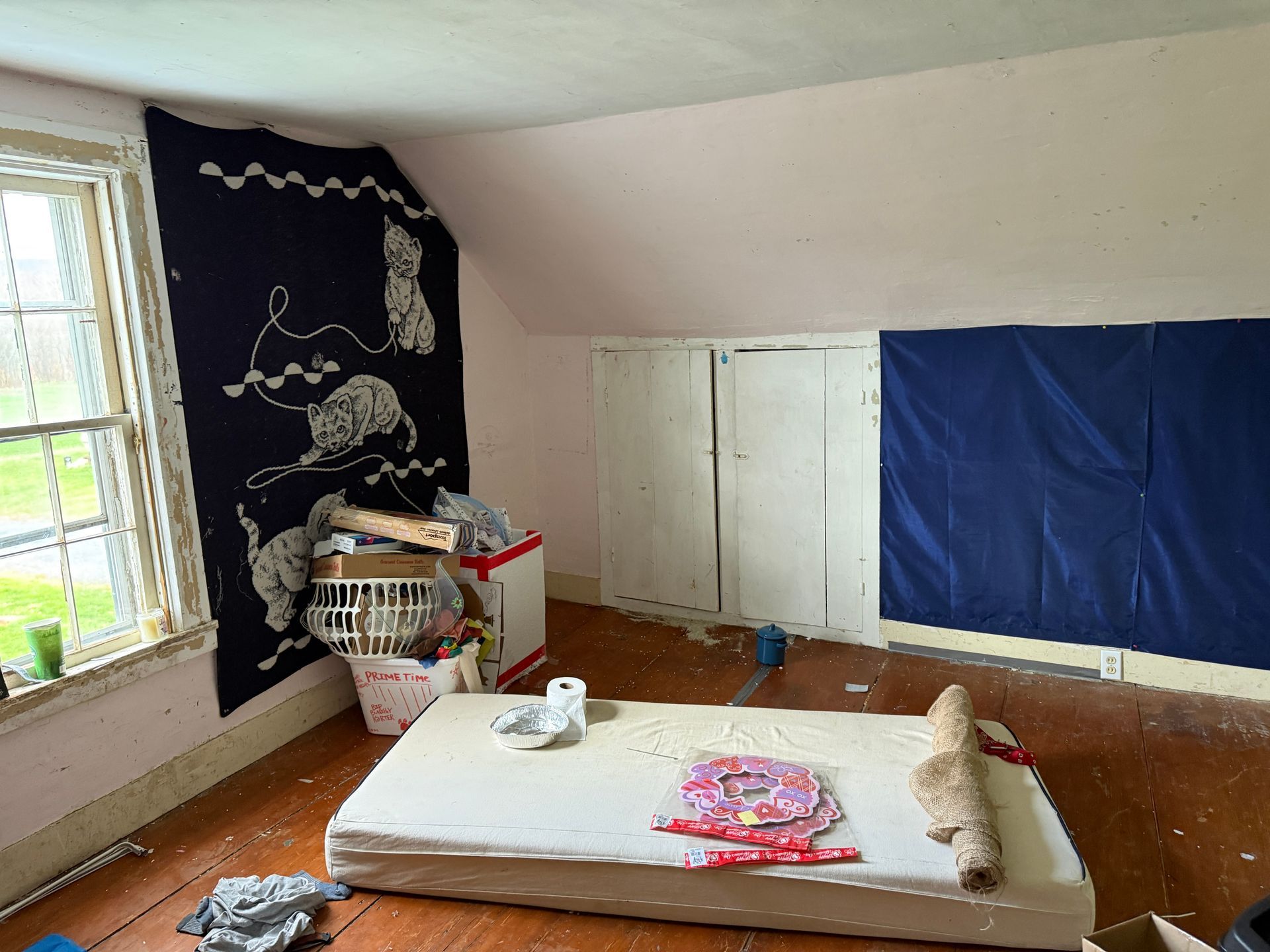 Attic room with mattress, window, and blue wall hanging.