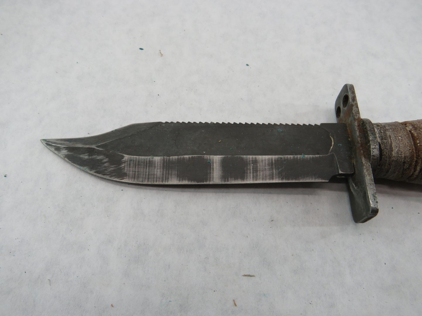 Close-up of a dark metal survival knife with serrated spine and wrapped handle.