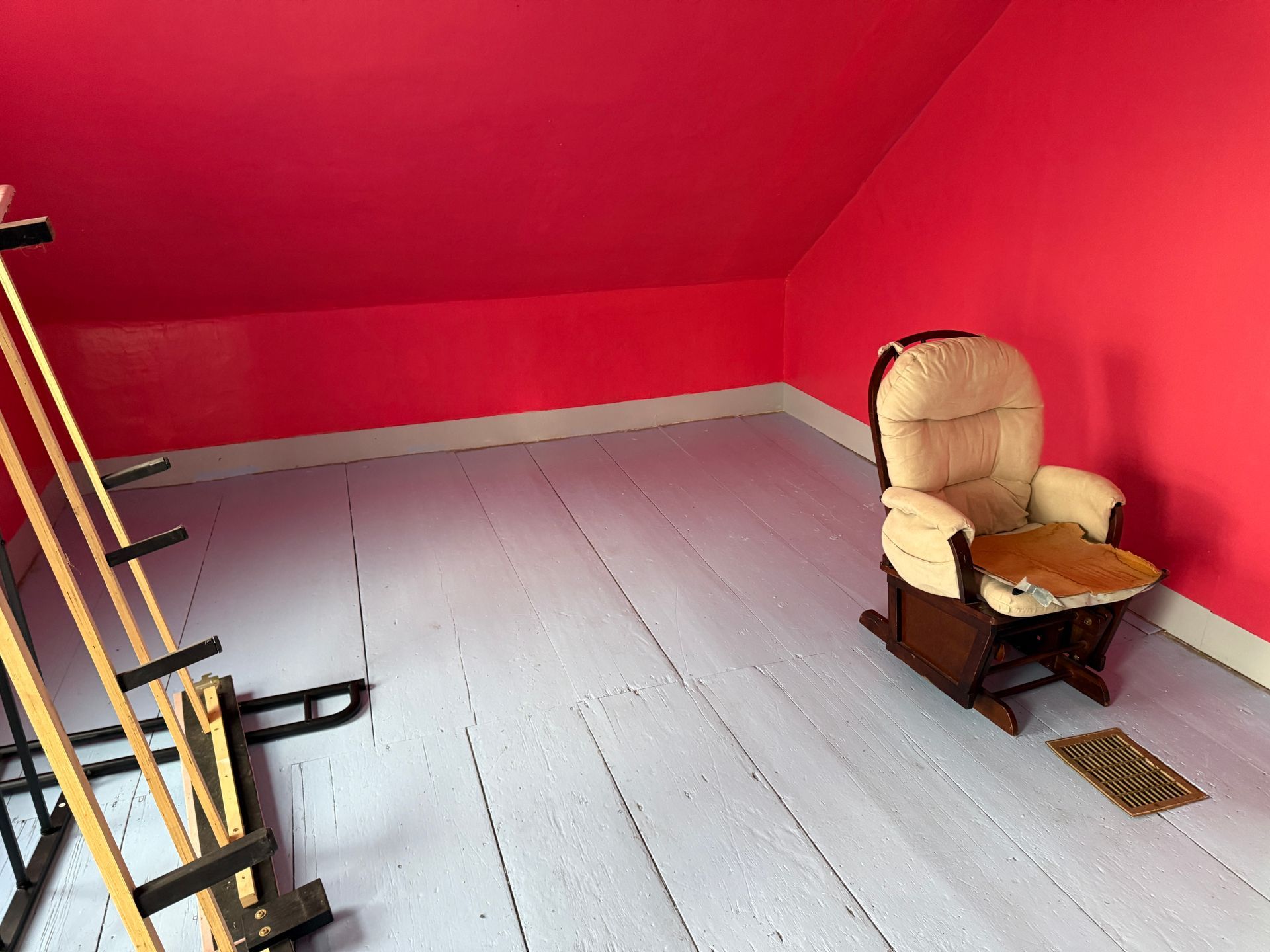 A small room with red walls, light wood floor, a rocking chair, and an easel.