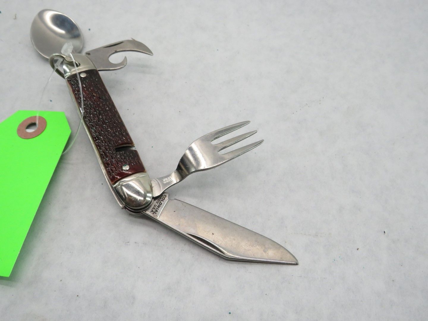Multi-tool camping utensil with spoon, fork, knife, and bottle opener, on a white surface.
