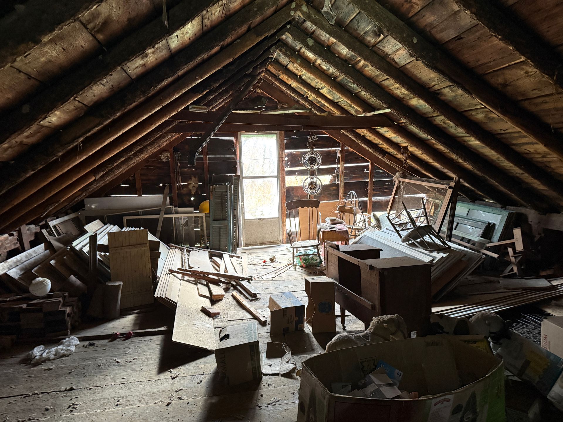 Attic with exposed wooden beams, a door, and various stored items.