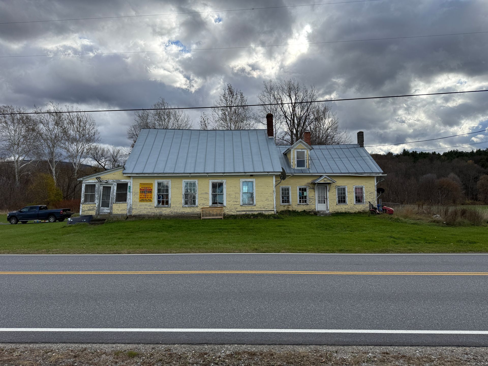 Yellow house with gray roof, along a road under a cloudy sky.