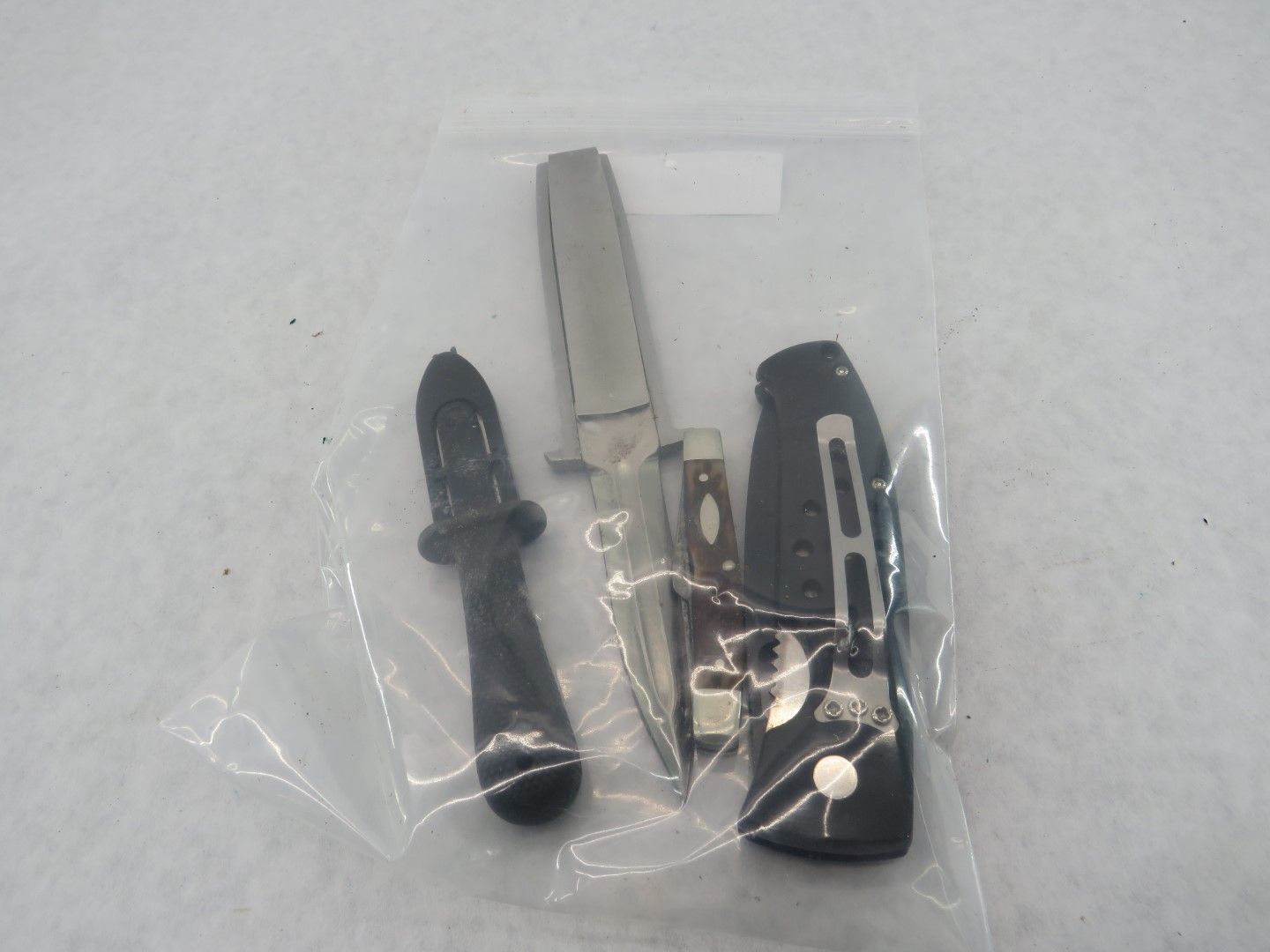Knives and sheath in a plastic bag. One black handle knife and one folding knife with a metal handle.