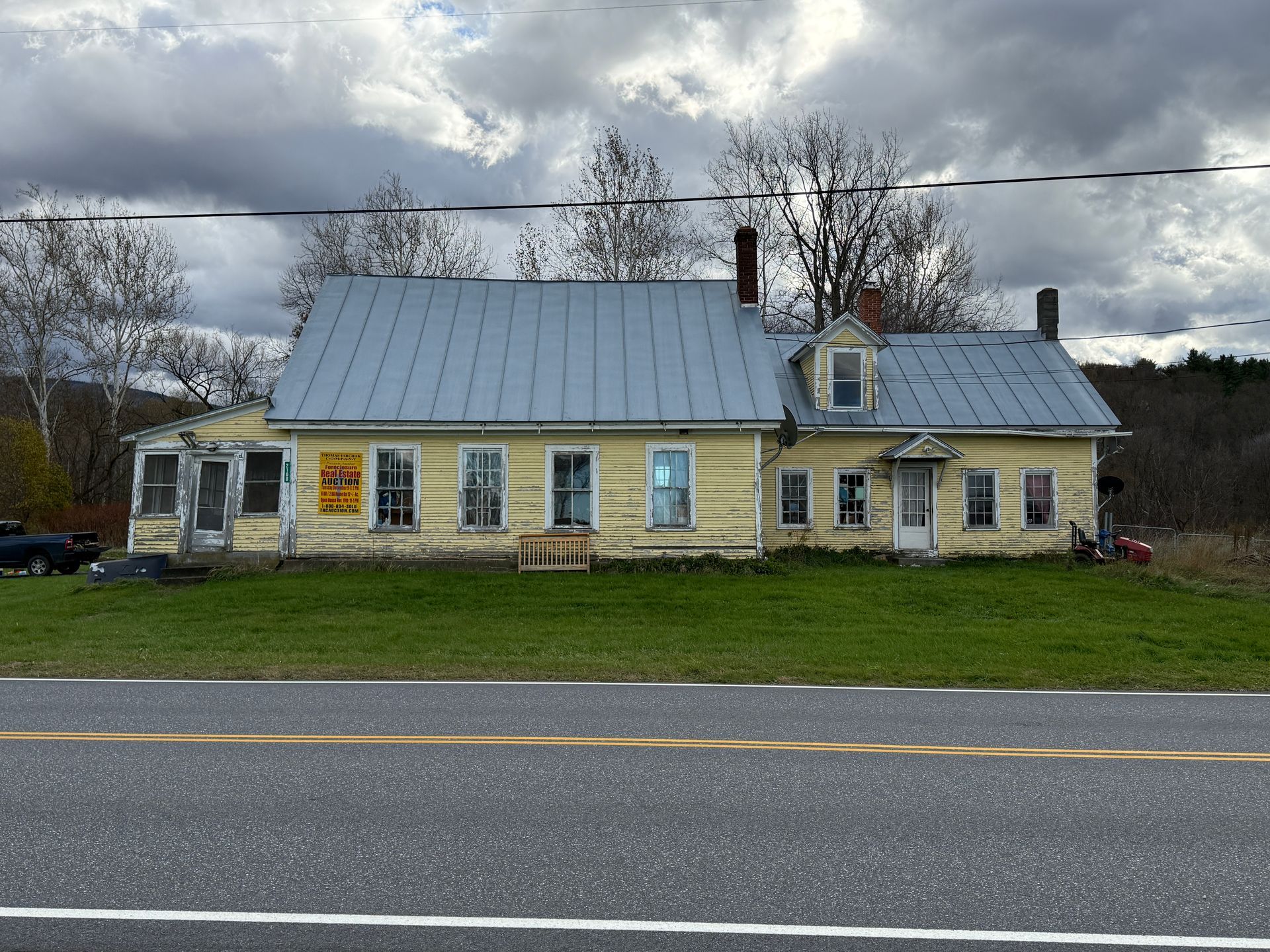 Yellow house with blue metal roof, next to a road, under a cloudy sky.