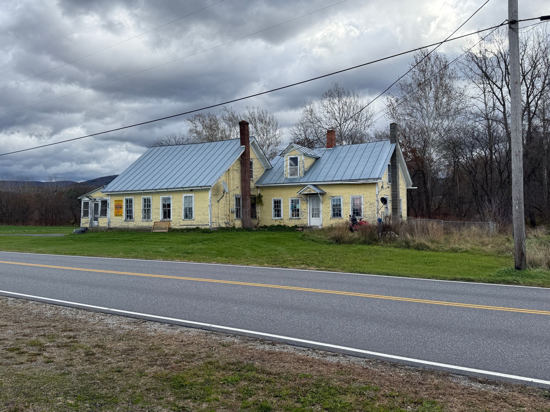 Yellow house with blue roof by a road on a cloudy day.