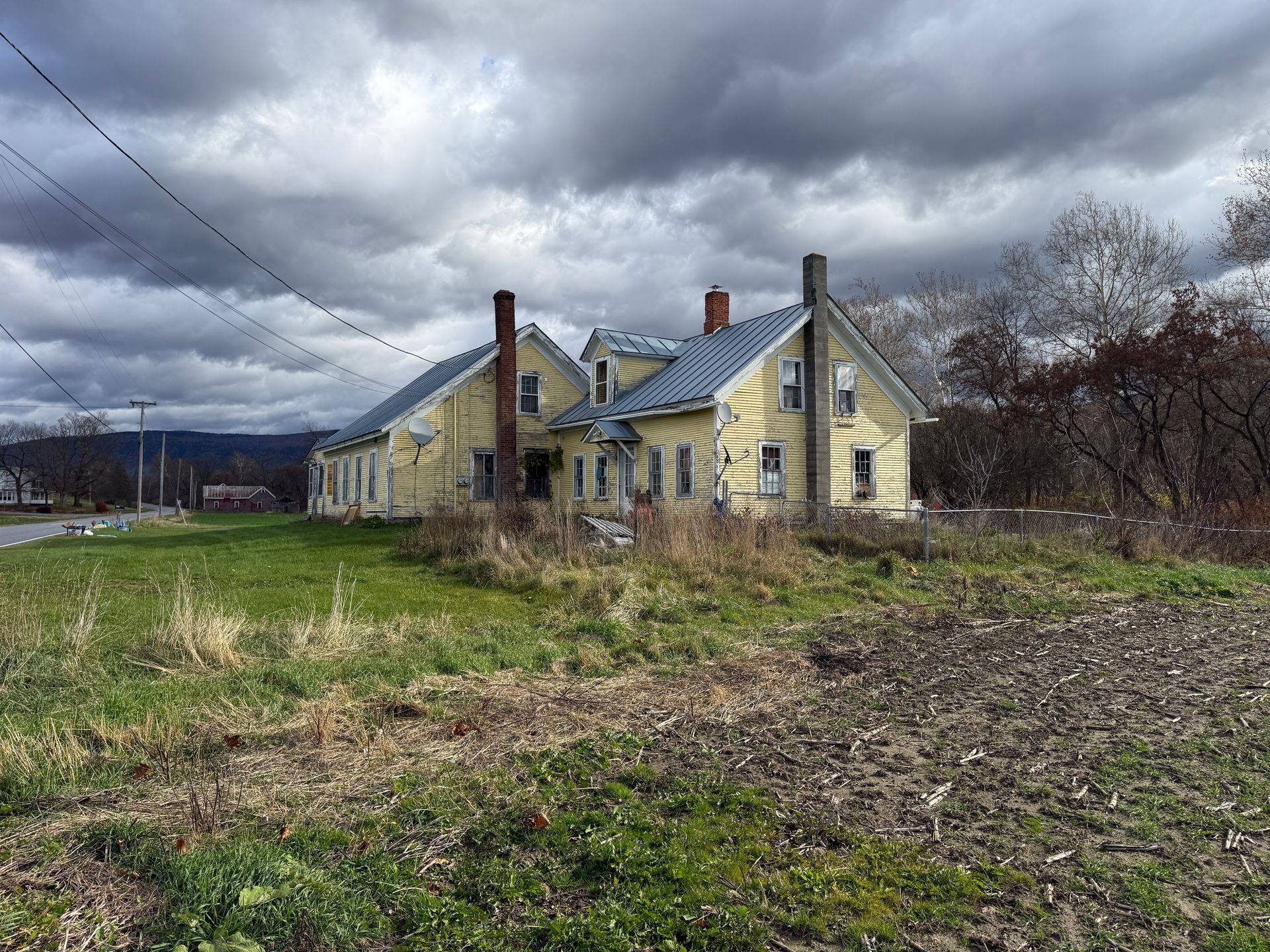Yellow house under a cloudy sky, with grass and dirt in the foreground.