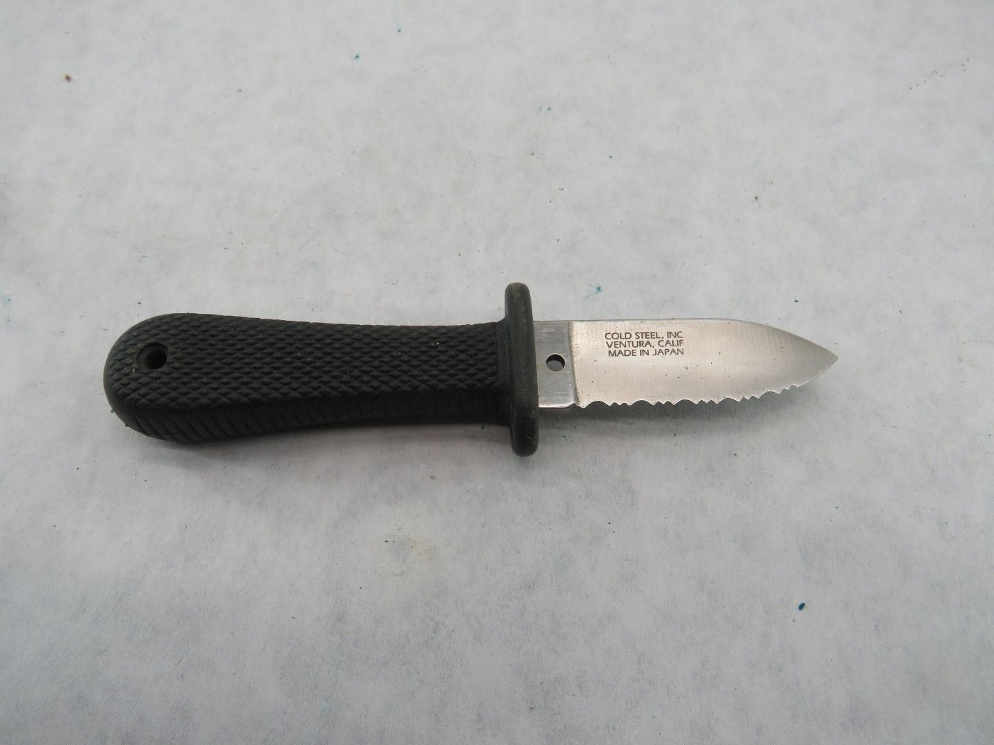 Black handled dive knife on a white surface with the blade pointing to the right.
