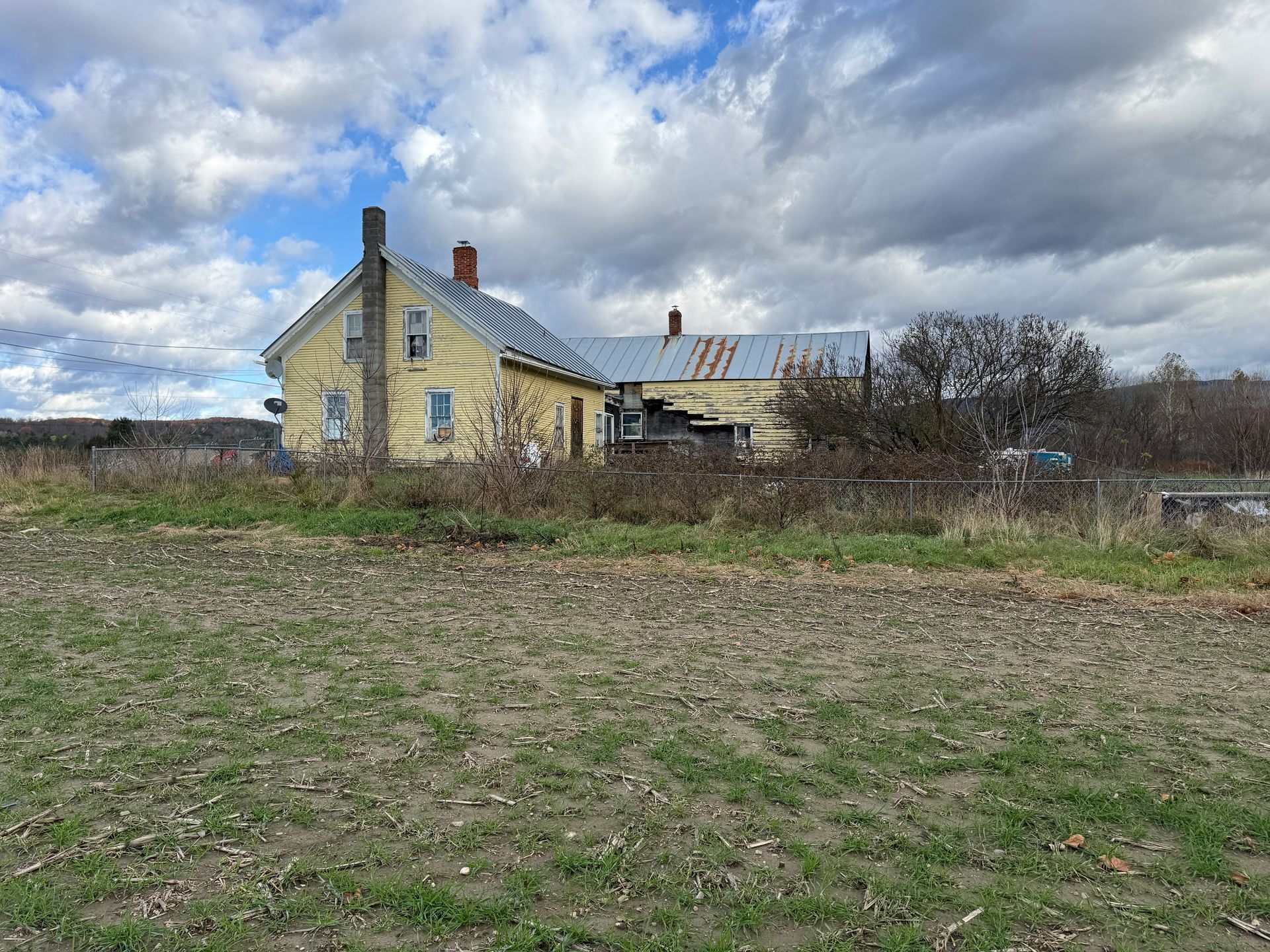 Yellow house with a tin roof under a cloudy sky.