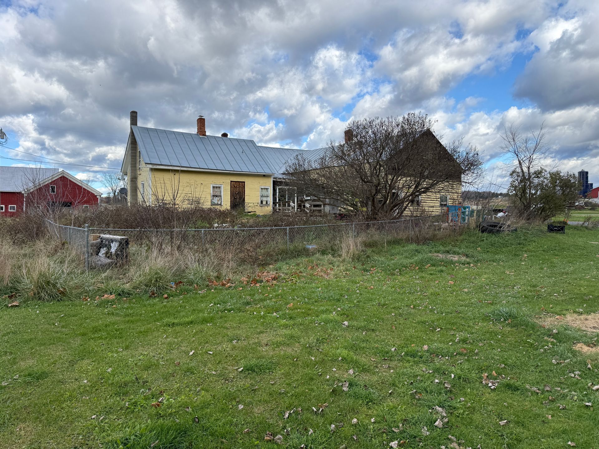 Yellow house with metal roof on a grassy field, cloudy sky.