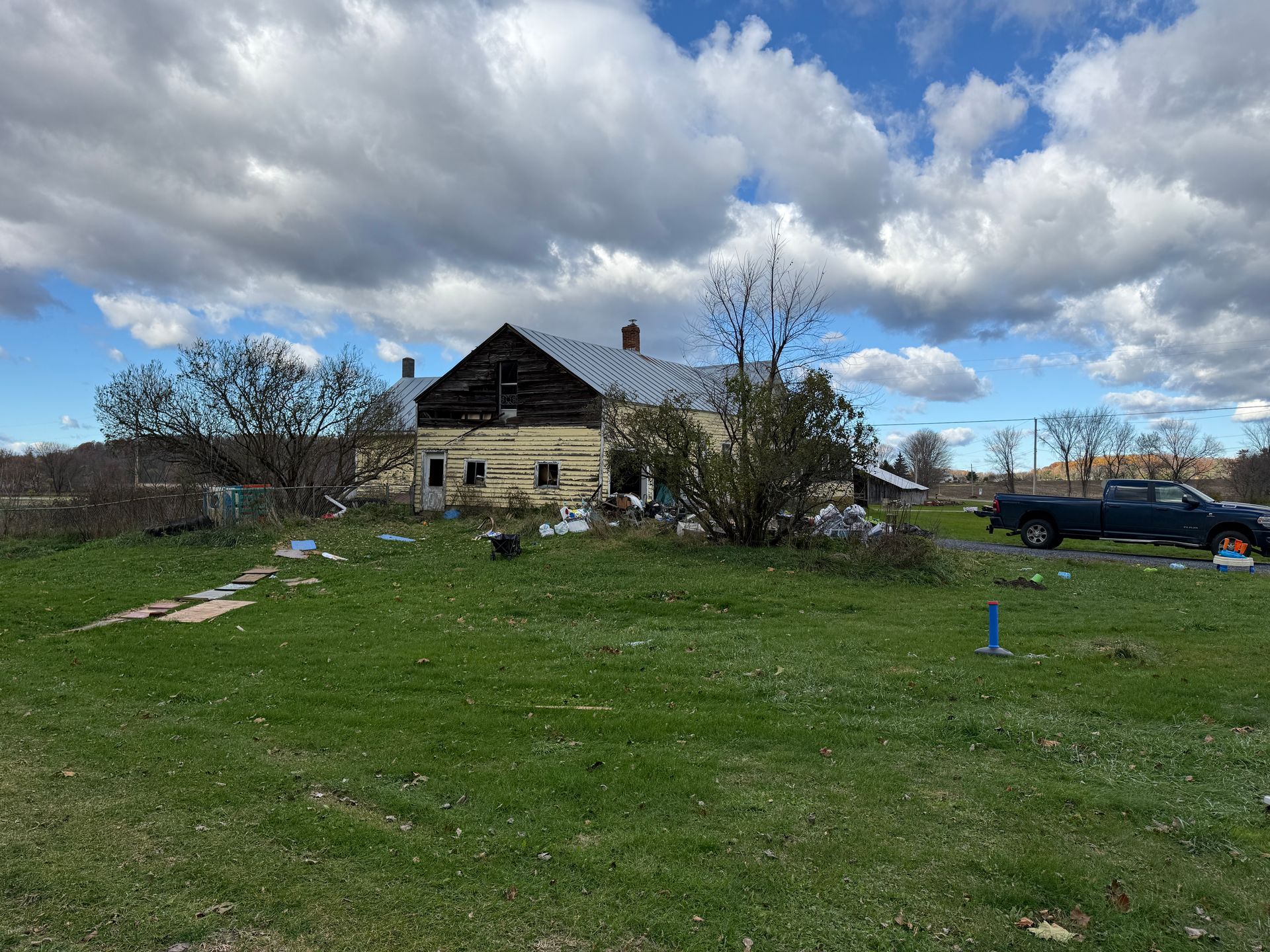 House with a grassy lot under a cloudy sky. A truck is parked nearby.