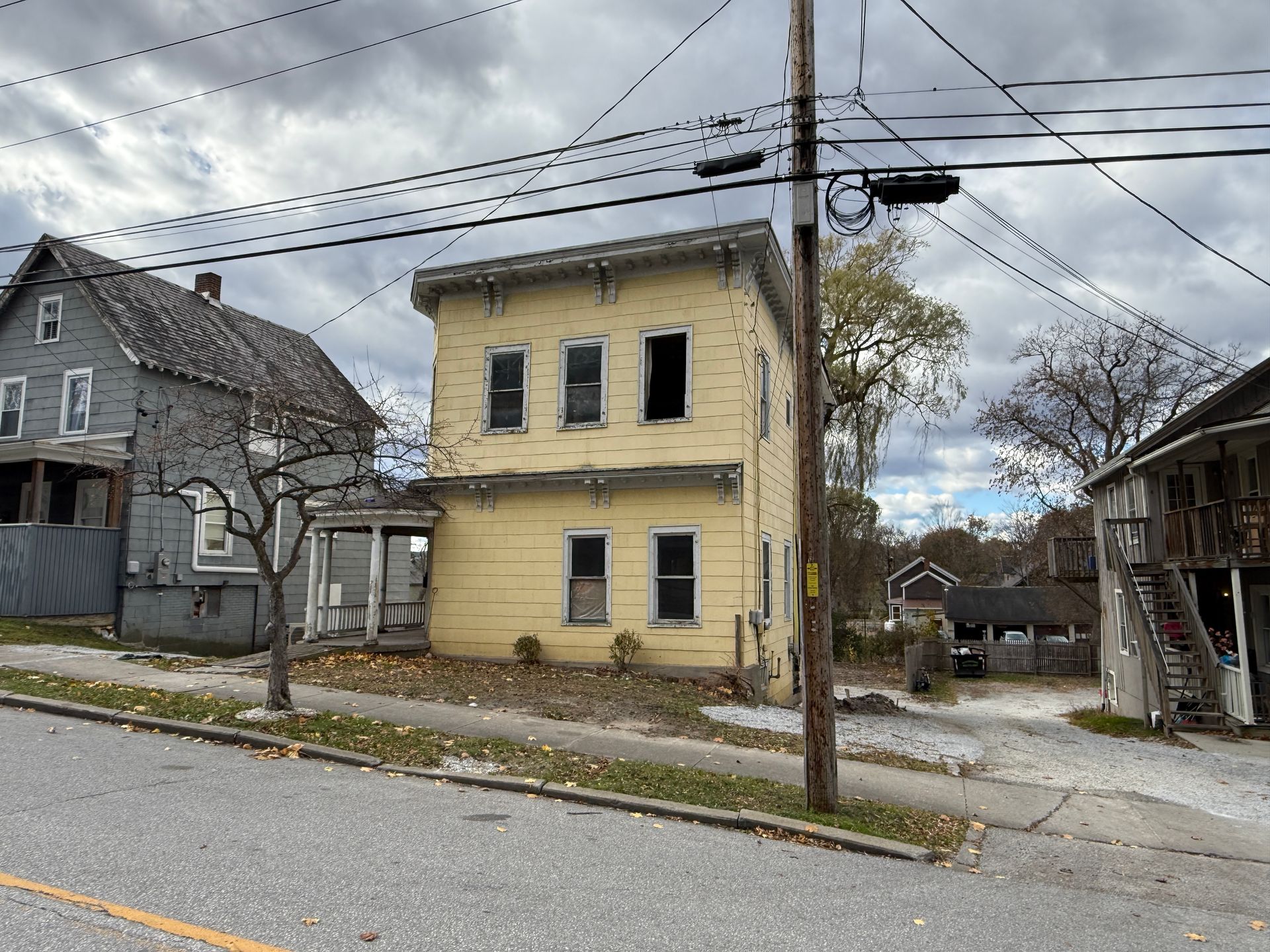 Two-story yellow house with street view with overcast sky.