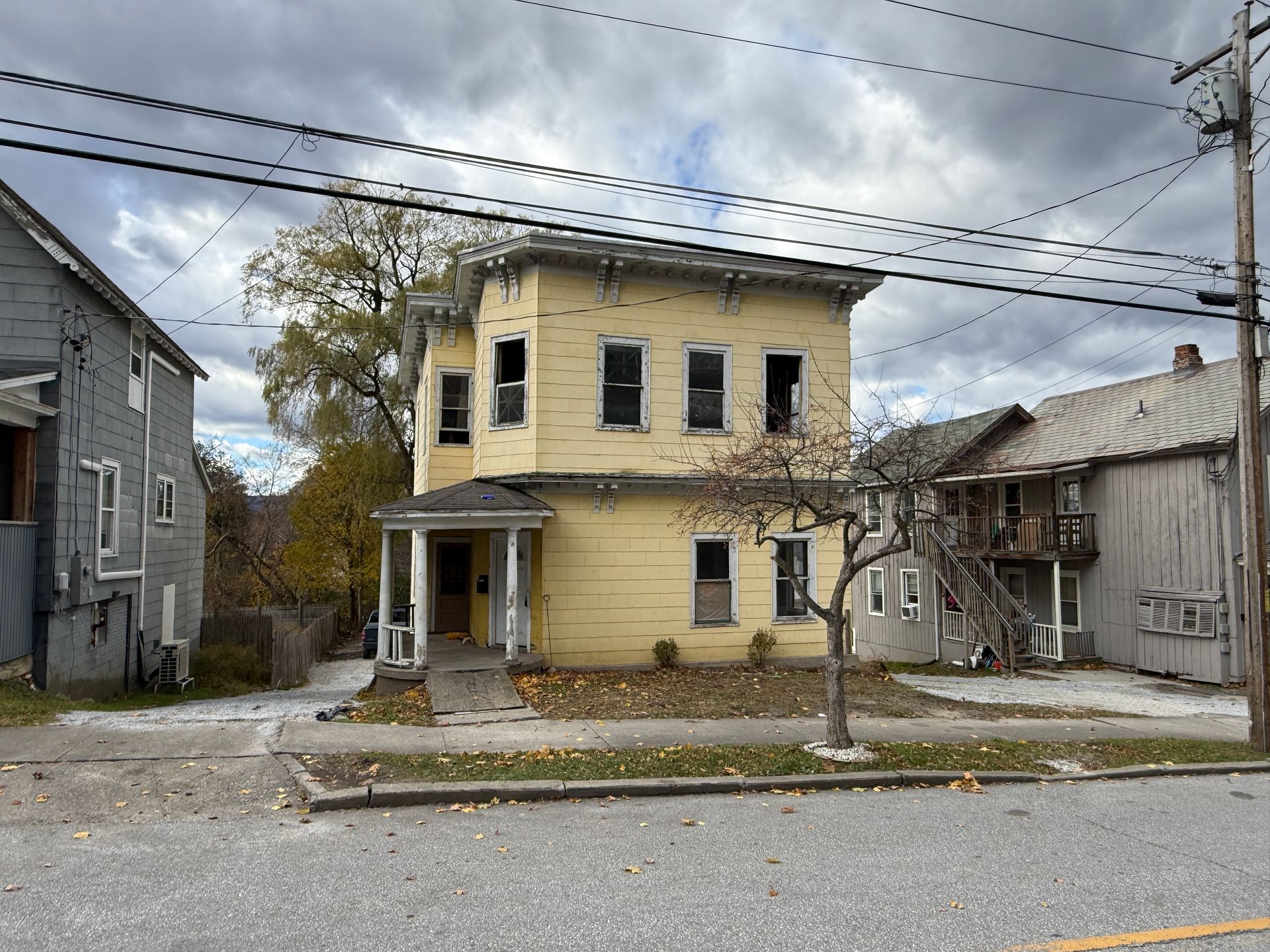 Two-story yellow house with porch, cloudy sky.
