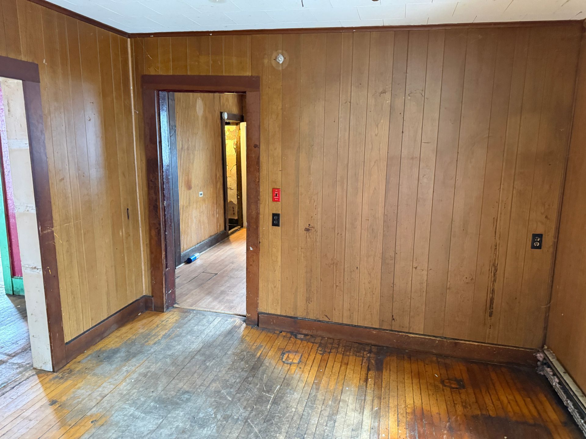 Empty room with wood paneling, doorway, and hardwood floors.