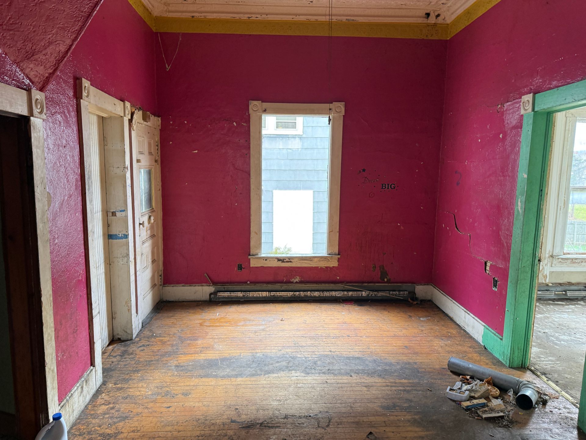Empty room with pink walls, a wooden floor, and a window.