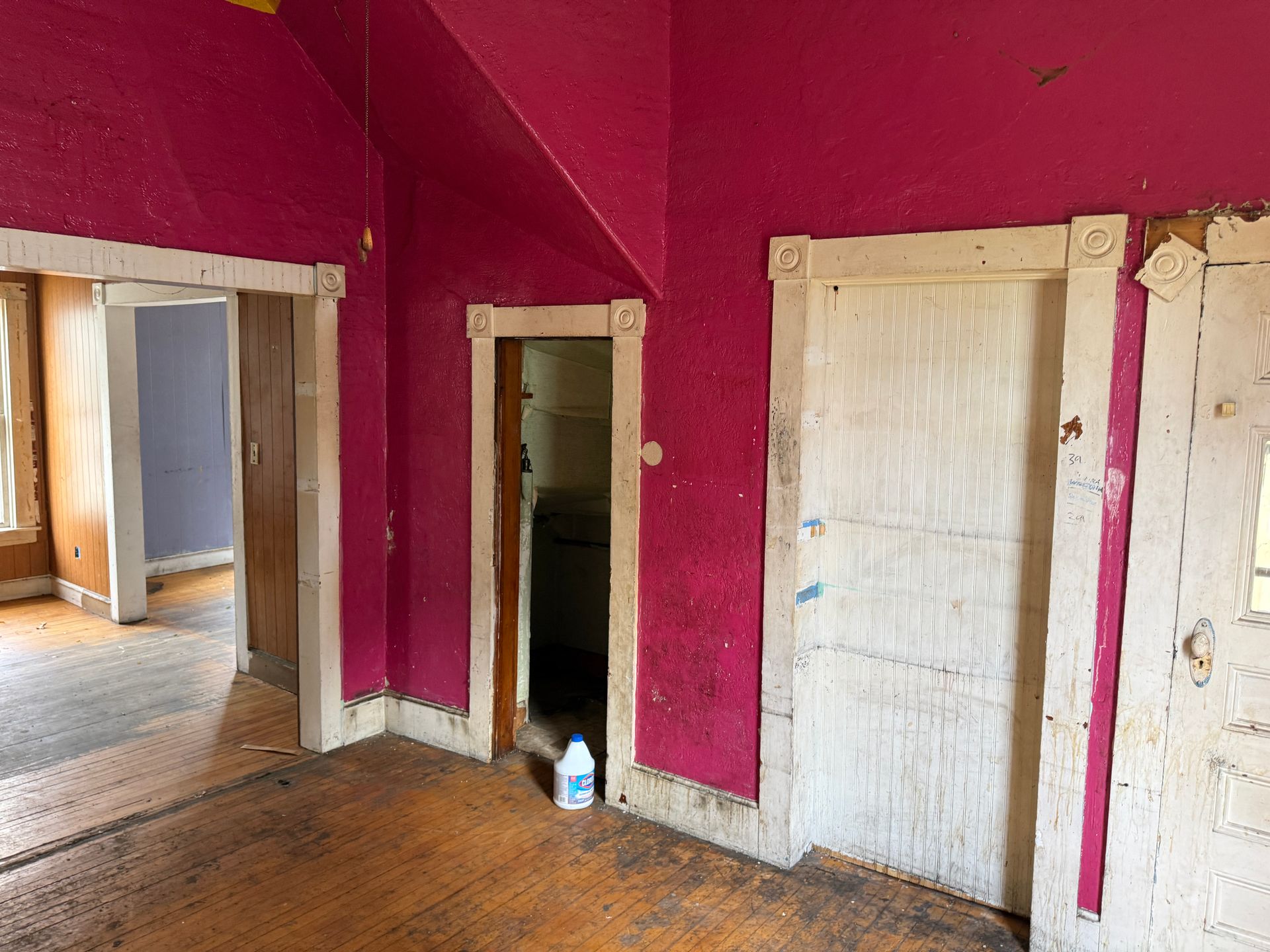 Interior room with bright pink walls, three doorways, and wooden floors.