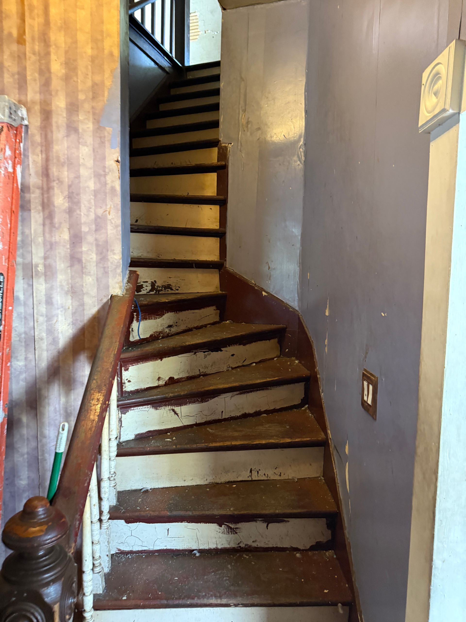 Narrow, wooden staircase curves upward with paint and handrail.