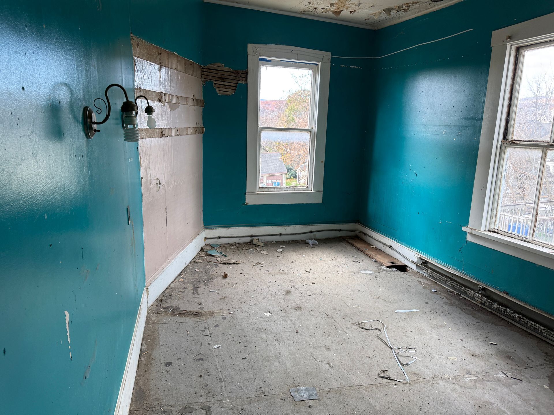Room with blue walls, two windows, and exposed wall sections.