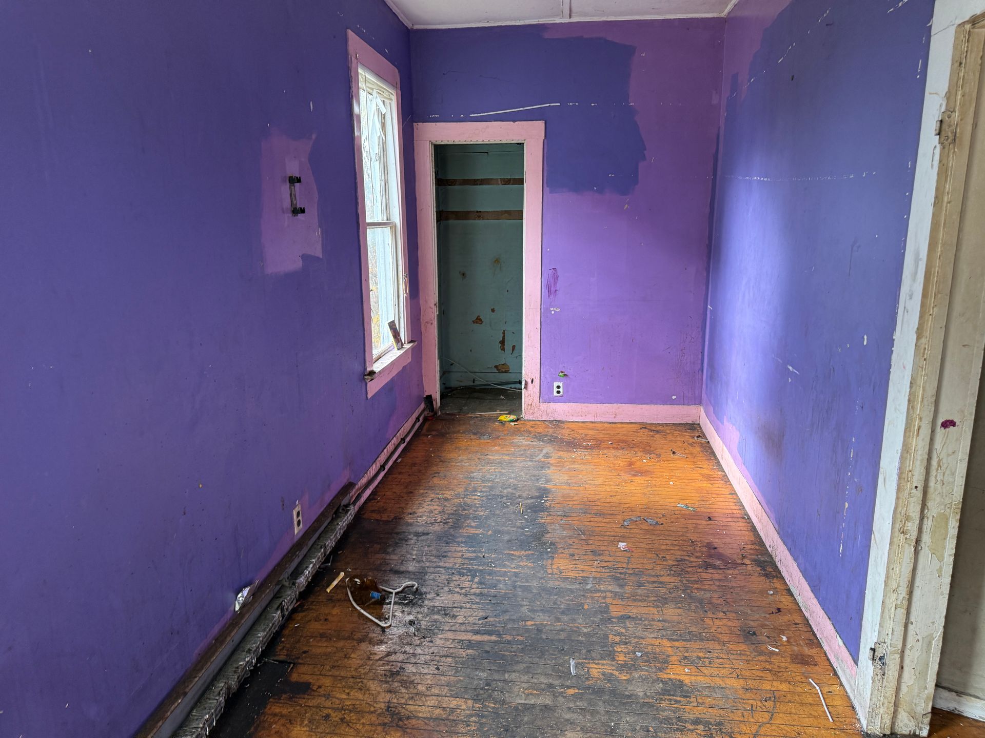 Purple-painted room with paint, wooden floor, window, and open closet.