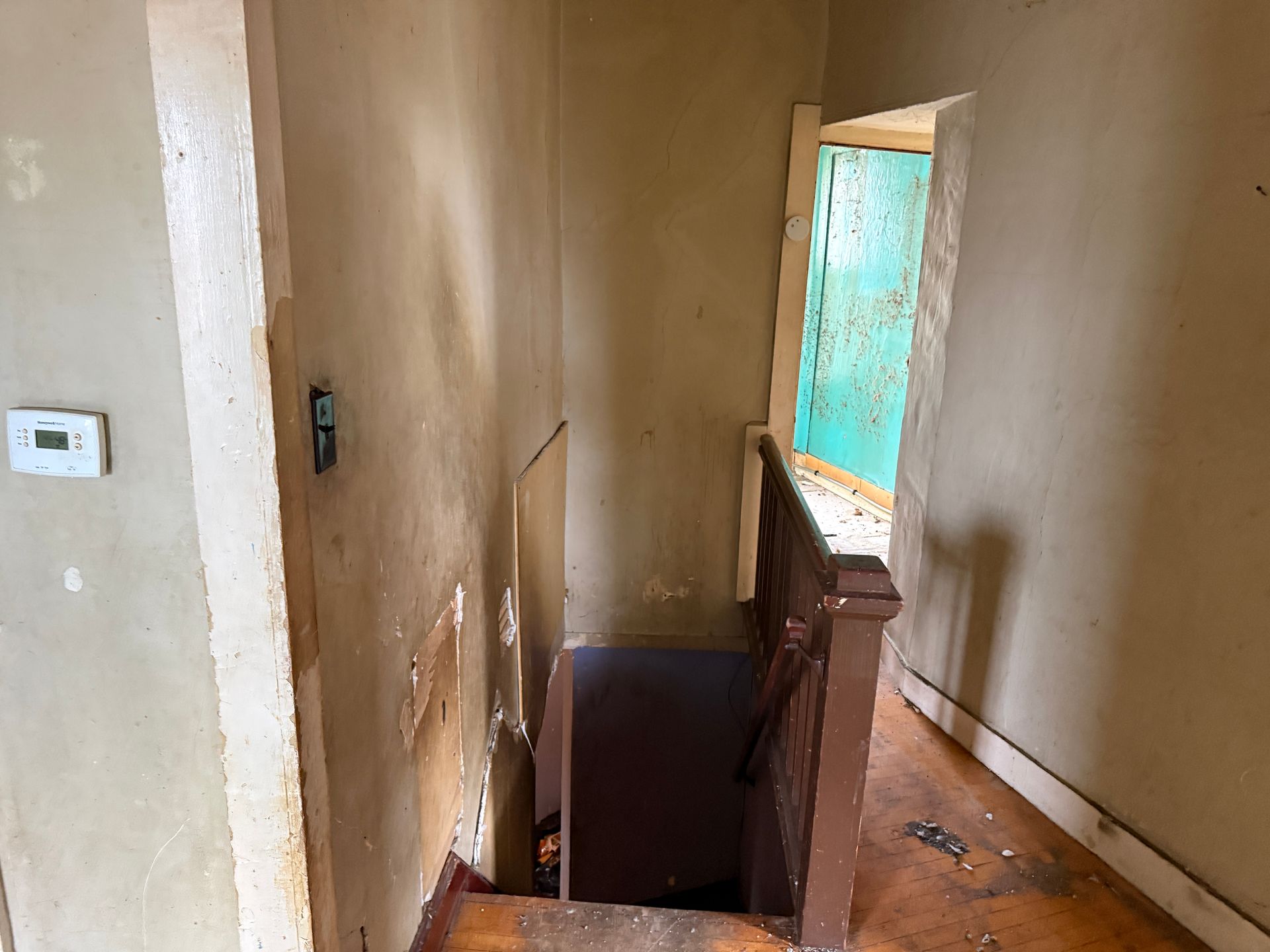 Stairwell with paint, a partially open turquoise door, and a brown banister.