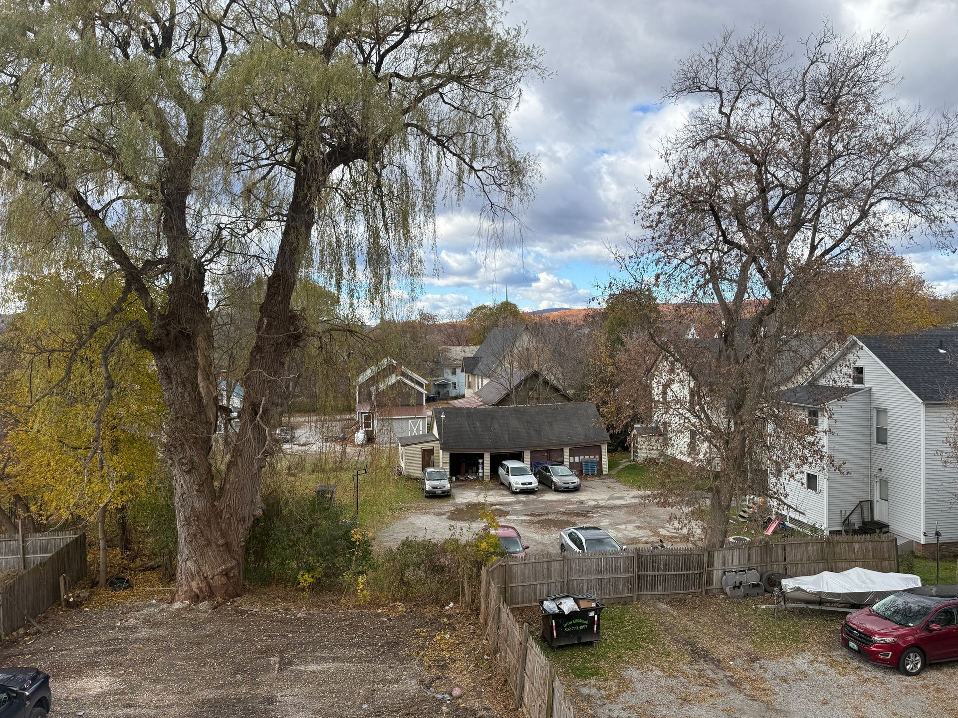 View overlooking a parking area with cars and a garage, trees in the foreground, cloudy sky.
