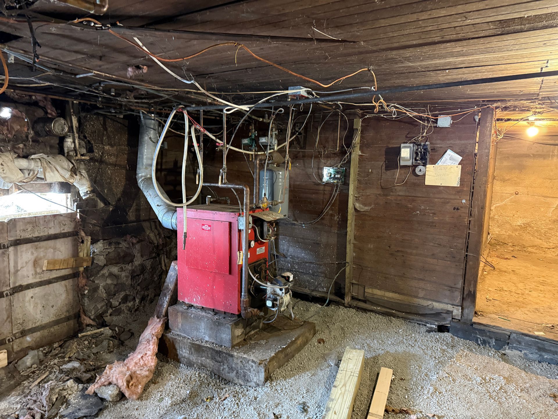 Basement with a red furnace, exposed wires, and wooden walls.