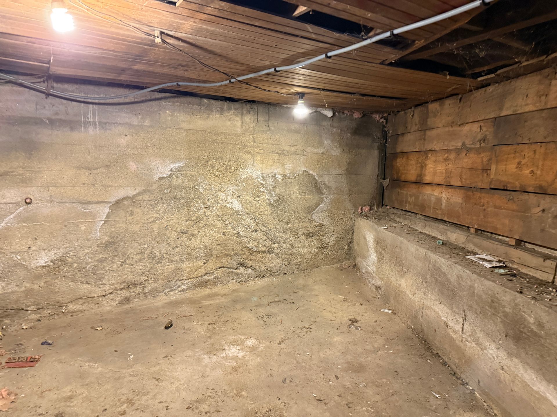 Concrete basement corner with exposed wood beams and wiring.