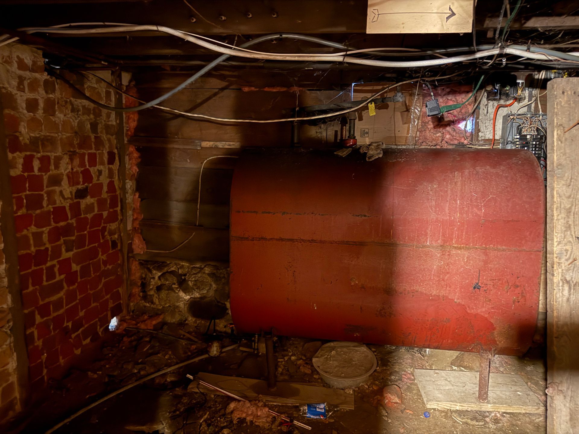 Red oil tank in a basement with brick walls, pipes, and wiring.