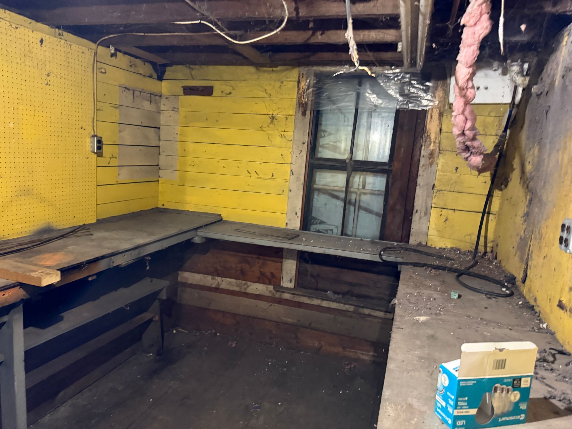 Yellow-painted basement room with workbench, window, electrical wiring, and plumbing.